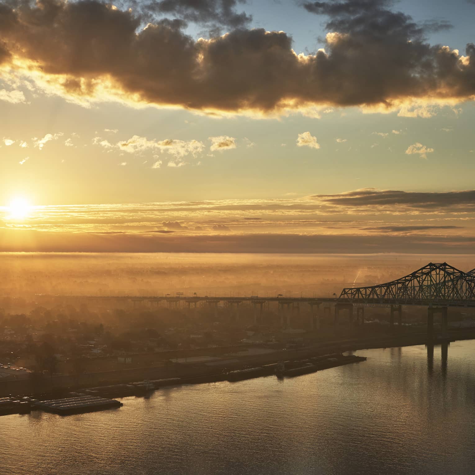 A sunrise near New Orleans bridge crossing a river.