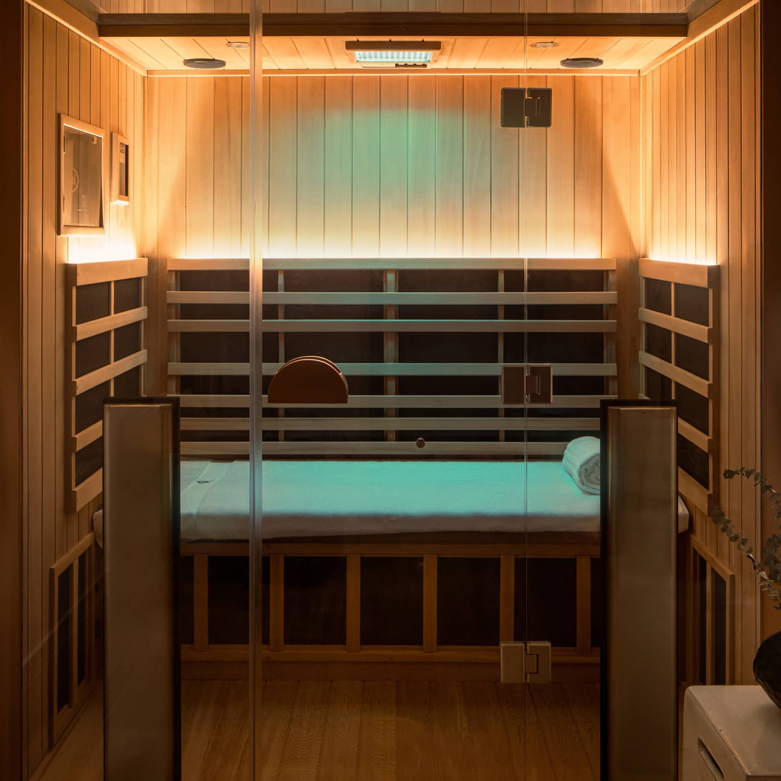 Wooden infrared sauna with lowlighting, side table with vase of eucalyptus 