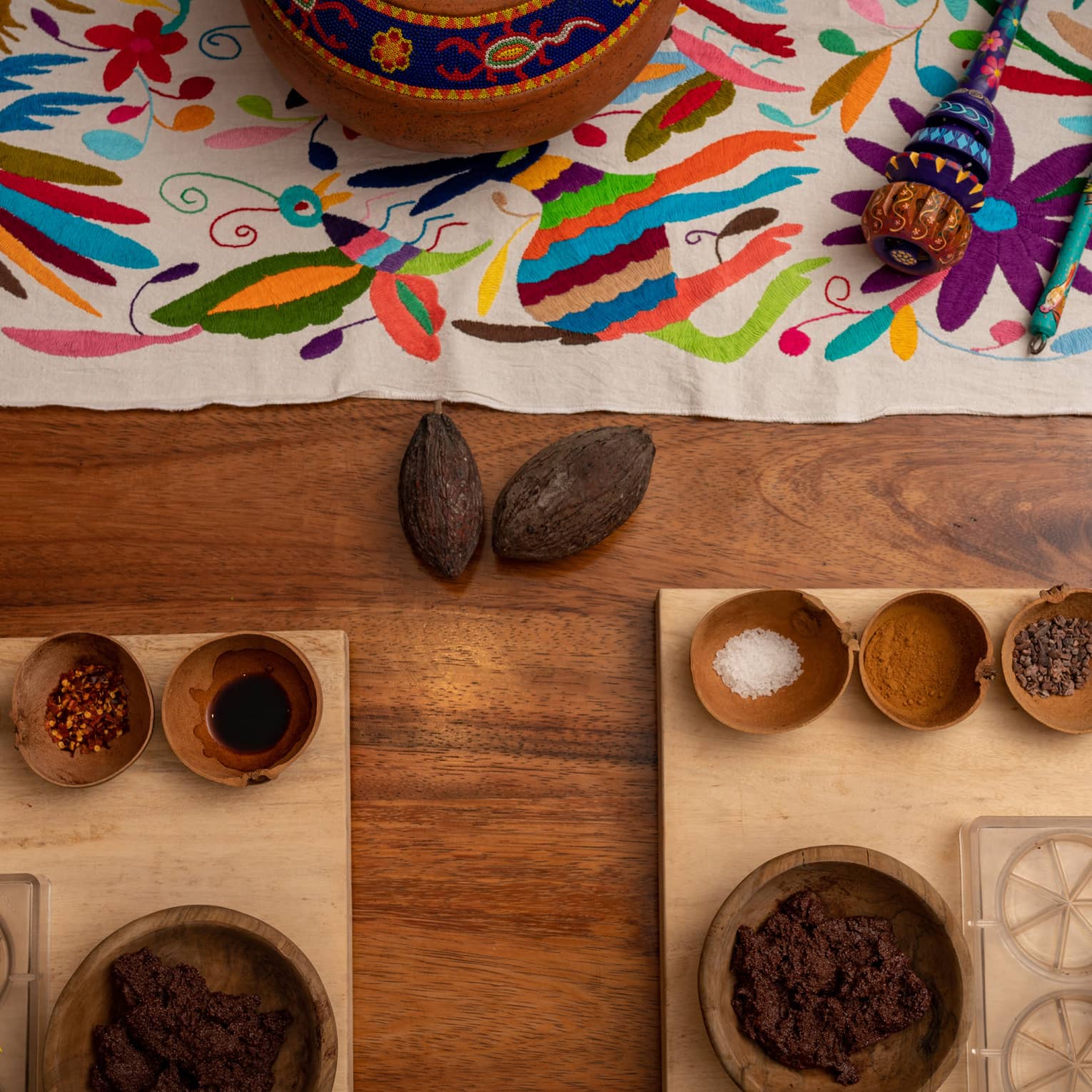 On a wooden surface, a bright tapestry, platters, bowls containing various ingredients, clear moulds and mixing tools.