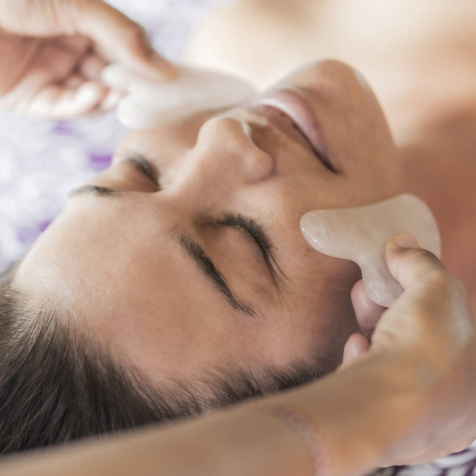 Hands hold stones at woman's cheeks on spa table