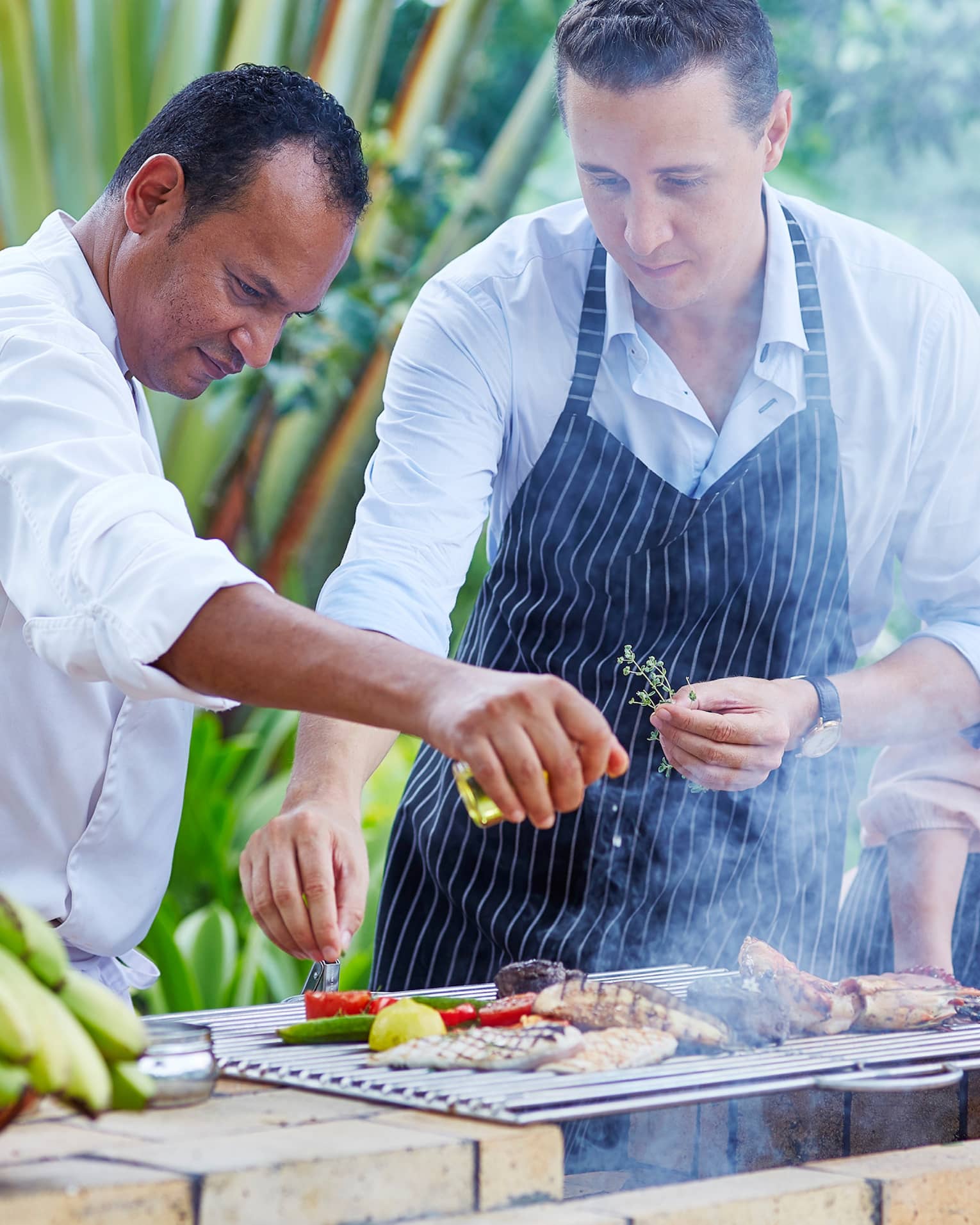 Chef, couple wearing aprons garnish meat, vegetables on outdoor grill