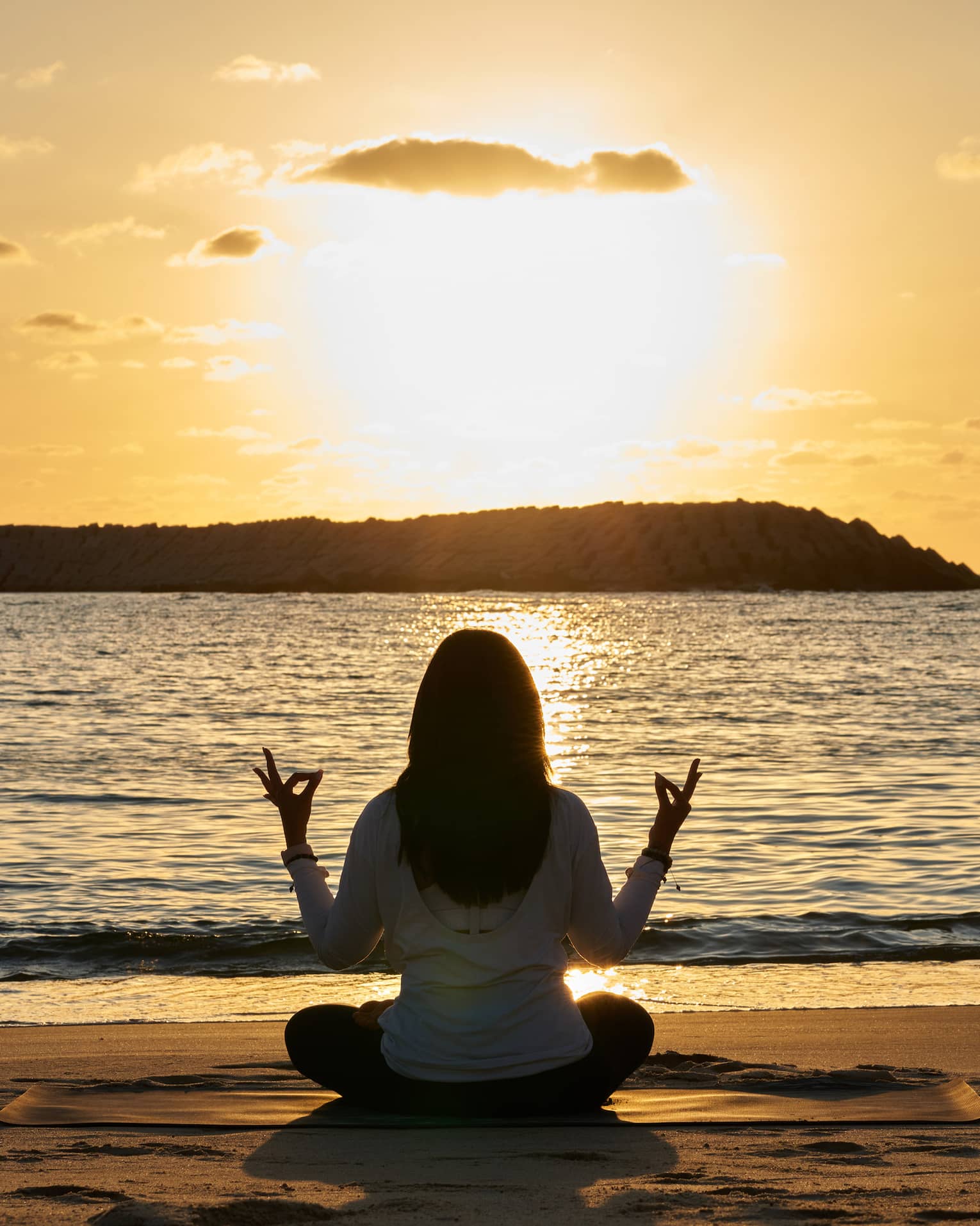 Woman meditates beachside at sunset