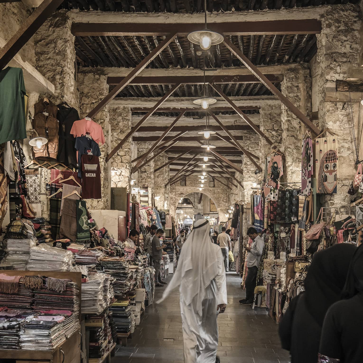 People walk past tables with textiles, clothes in indoor market