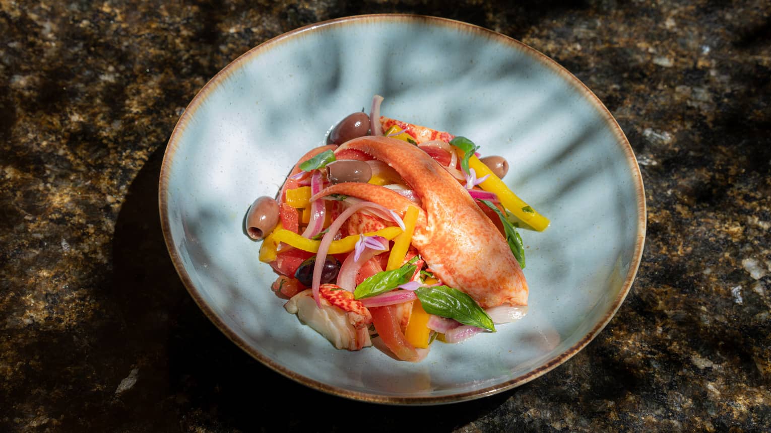 Octopus, lobster claw, olives and sliced onion in blue ceramic bowl