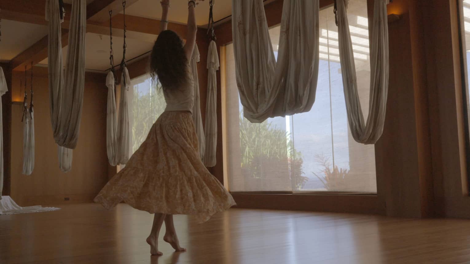 A woman dances in movement studio featuring hanging aerial yoga hammocks