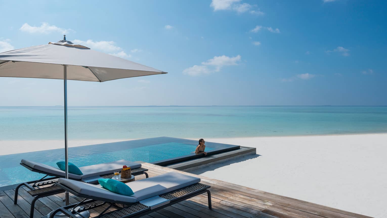 Woman leans against ledge of private infinity pool off Beach Villa patio, beach