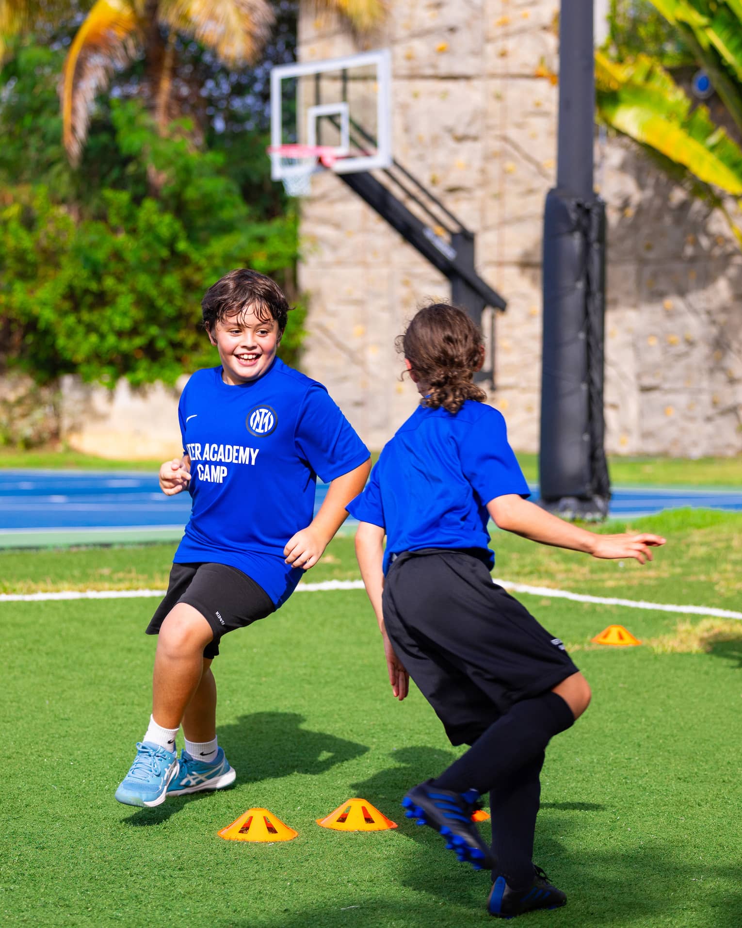 Soccer coach talking to two young guests exercising outside with a basketball court in the background.