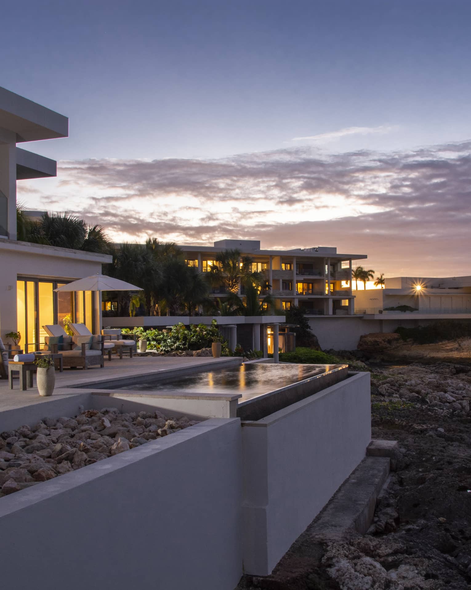 The exterior of a beachside hotel with orange lights coming from floor to ceiling windows.