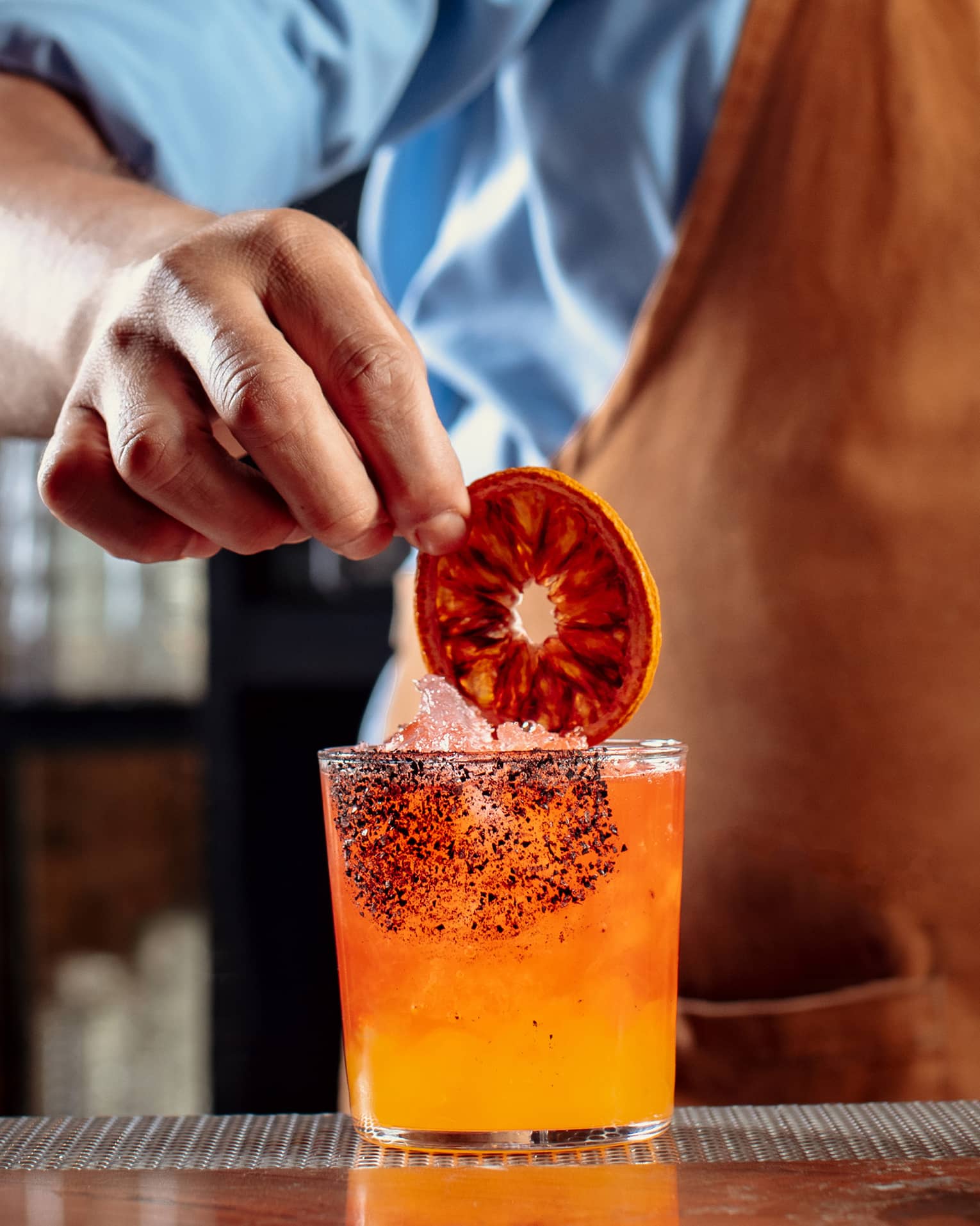 A bartender making an orange cocktail and putting a dark orange wheel in it.