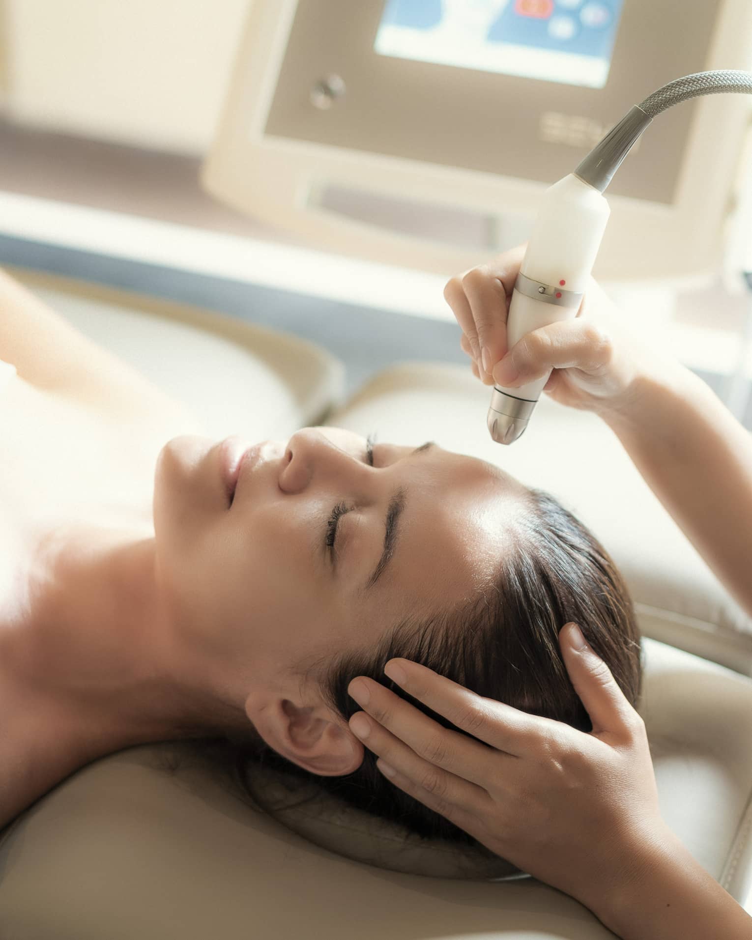 An aesthetician uses a tool on the face of a relaxing woman.