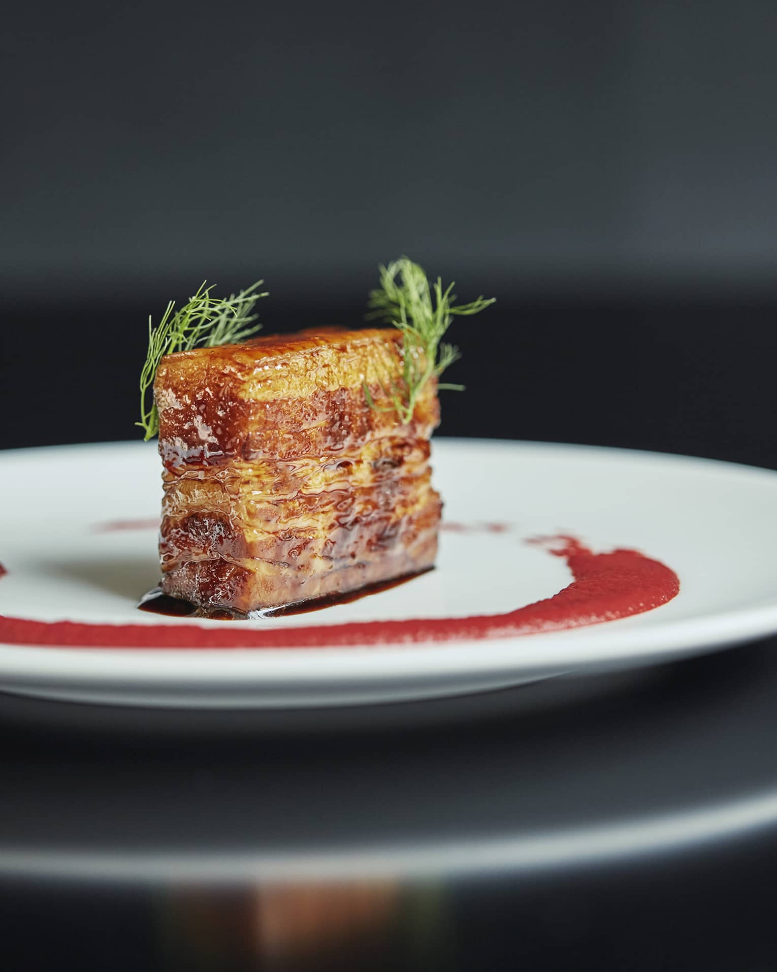 Pork belly slab on white plate with red sauce and green garnishes