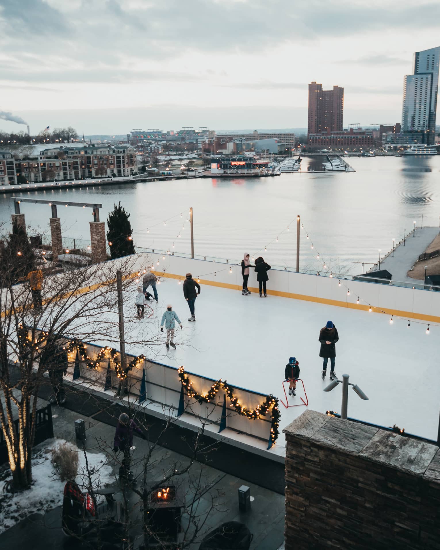 Aerial view of people ice skating at an outdoor ice rink beside a river.