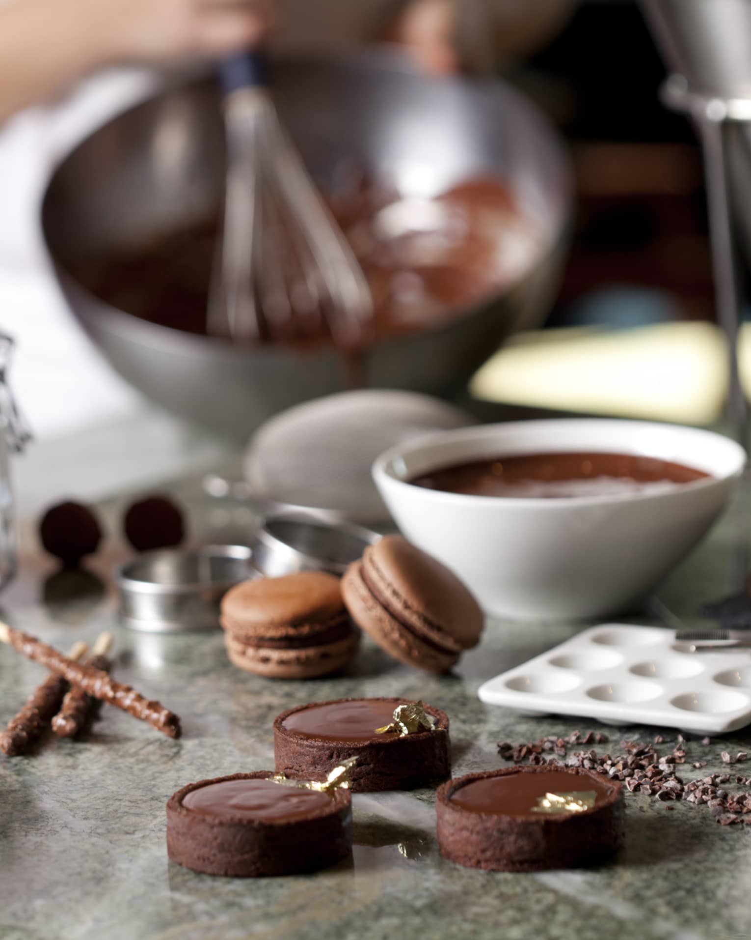Close-up of fine chocolates, macarons, bowl of melted chocolate on counter