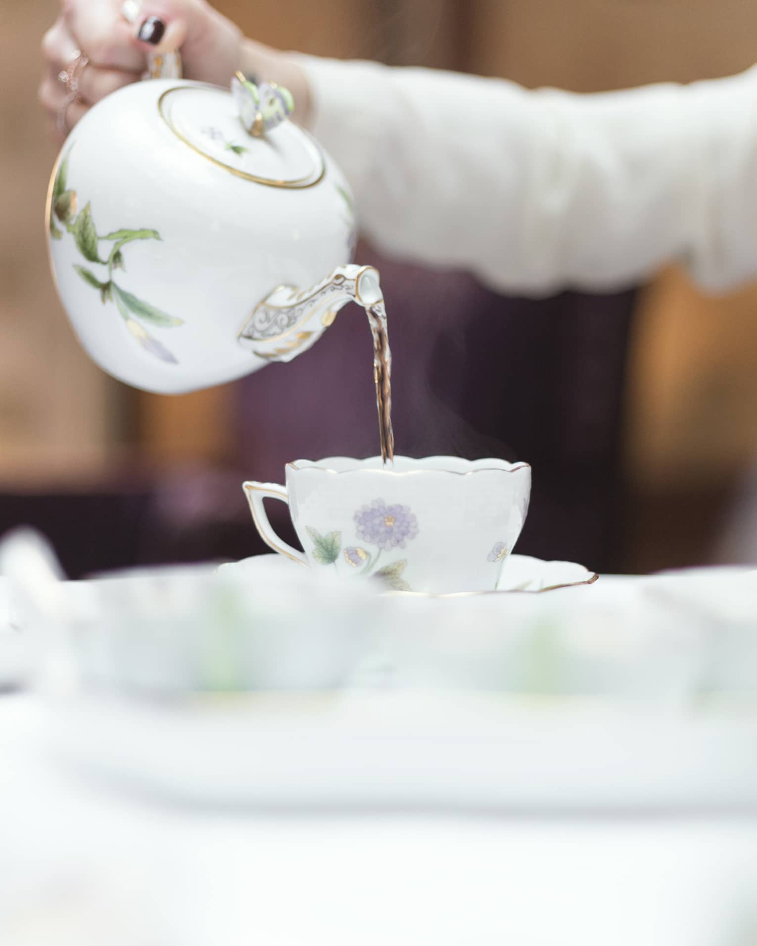 Person holds floral tea pot and pours tea into cup and saucer 