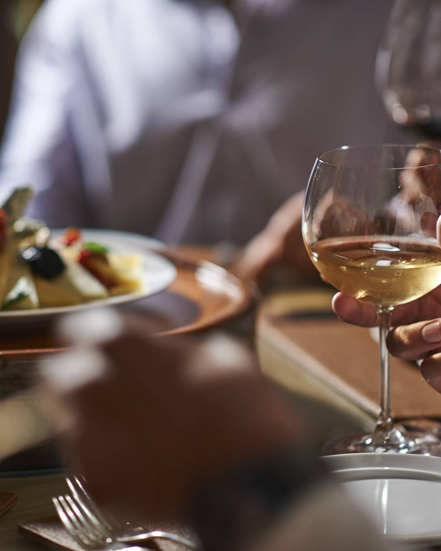 Close-up of hand holding wine glass by dinner plate on table
