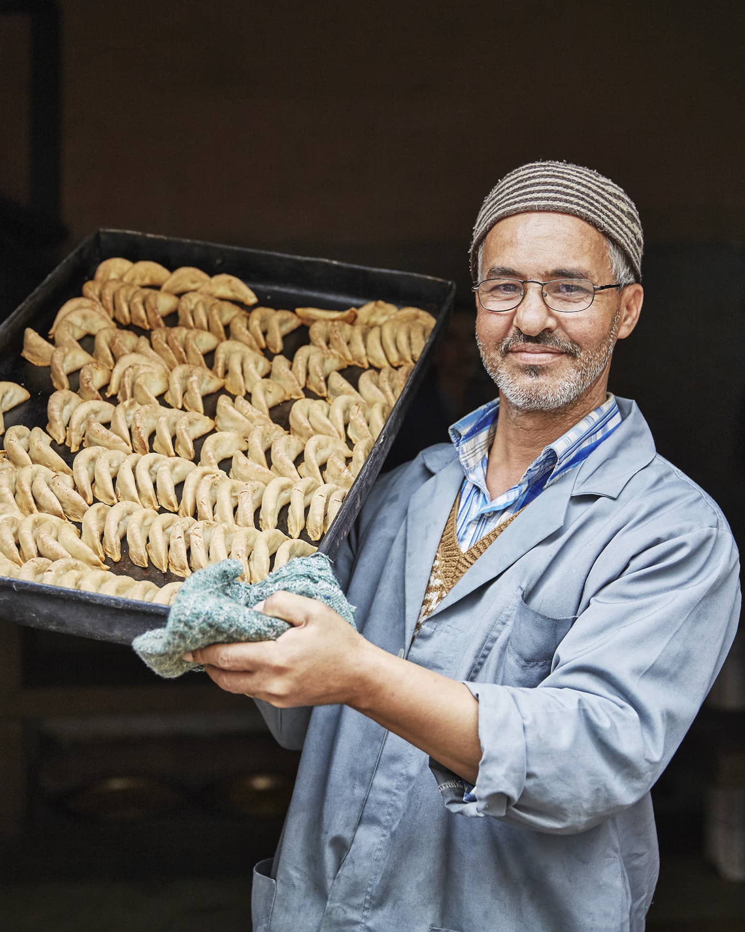 Pastry chef in casual blue coat, hats holds tray with crescent-shaped corned de gazelle