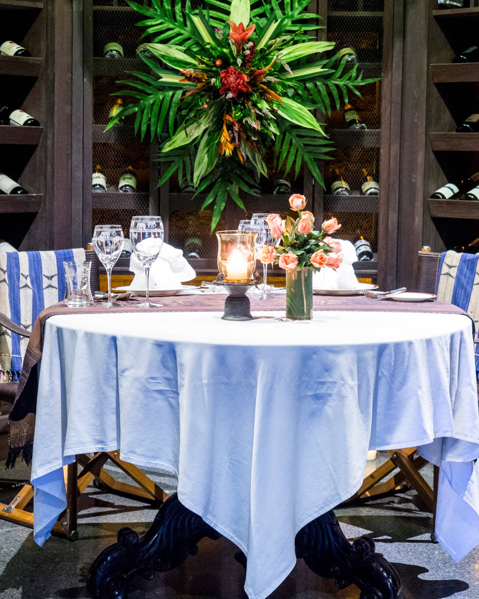 Round dining table with white cloth set with wine glasses, flowers in wine cellar enclave