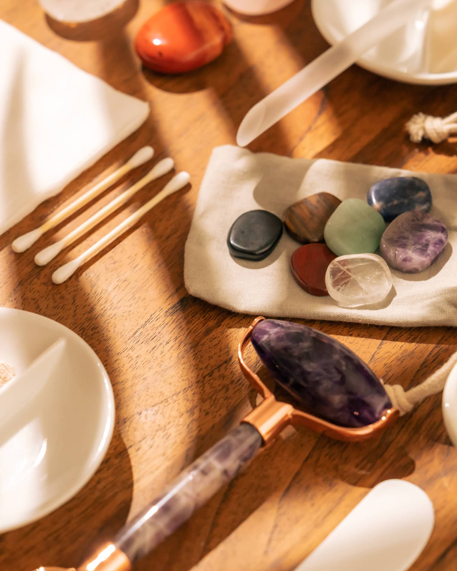 Face roller, gemstones, cotton swabs and a variety of small white bowls and other instruments sit on a sun-lit wooden table