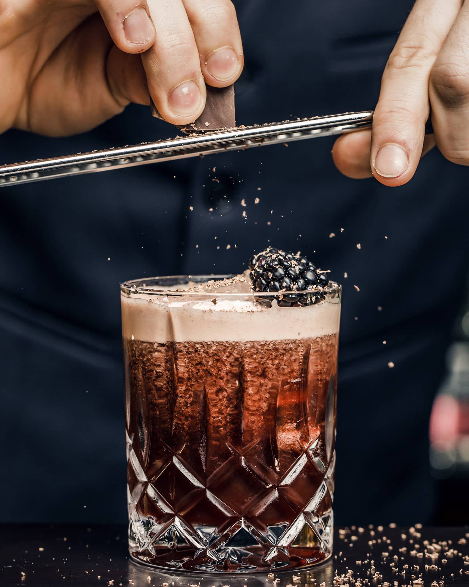 Churchill Club bartender shaves garnish over cocktail in crystal rock glass with blackberry