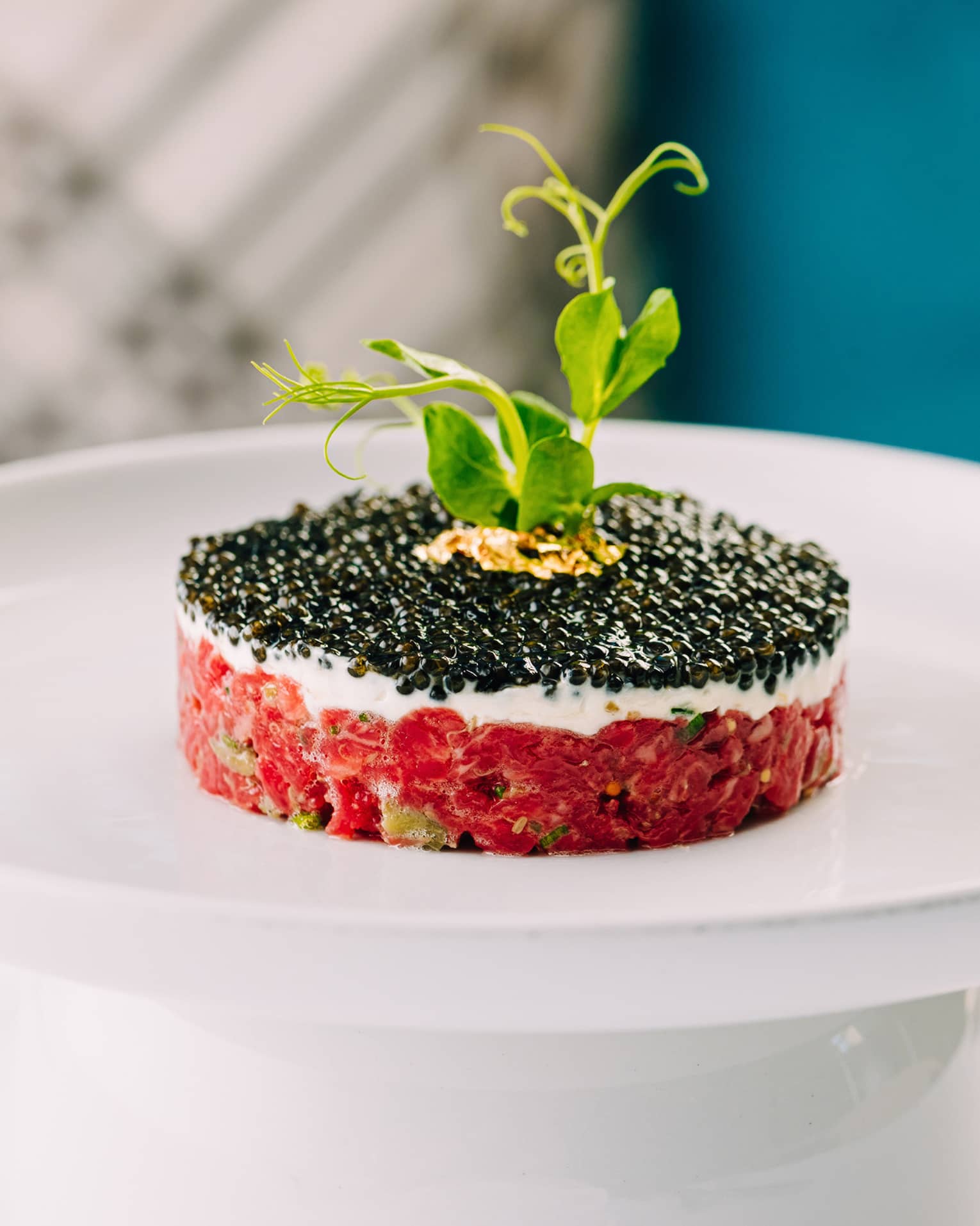 A circular tartare covered in caviar with a sprig of parsley on top. 