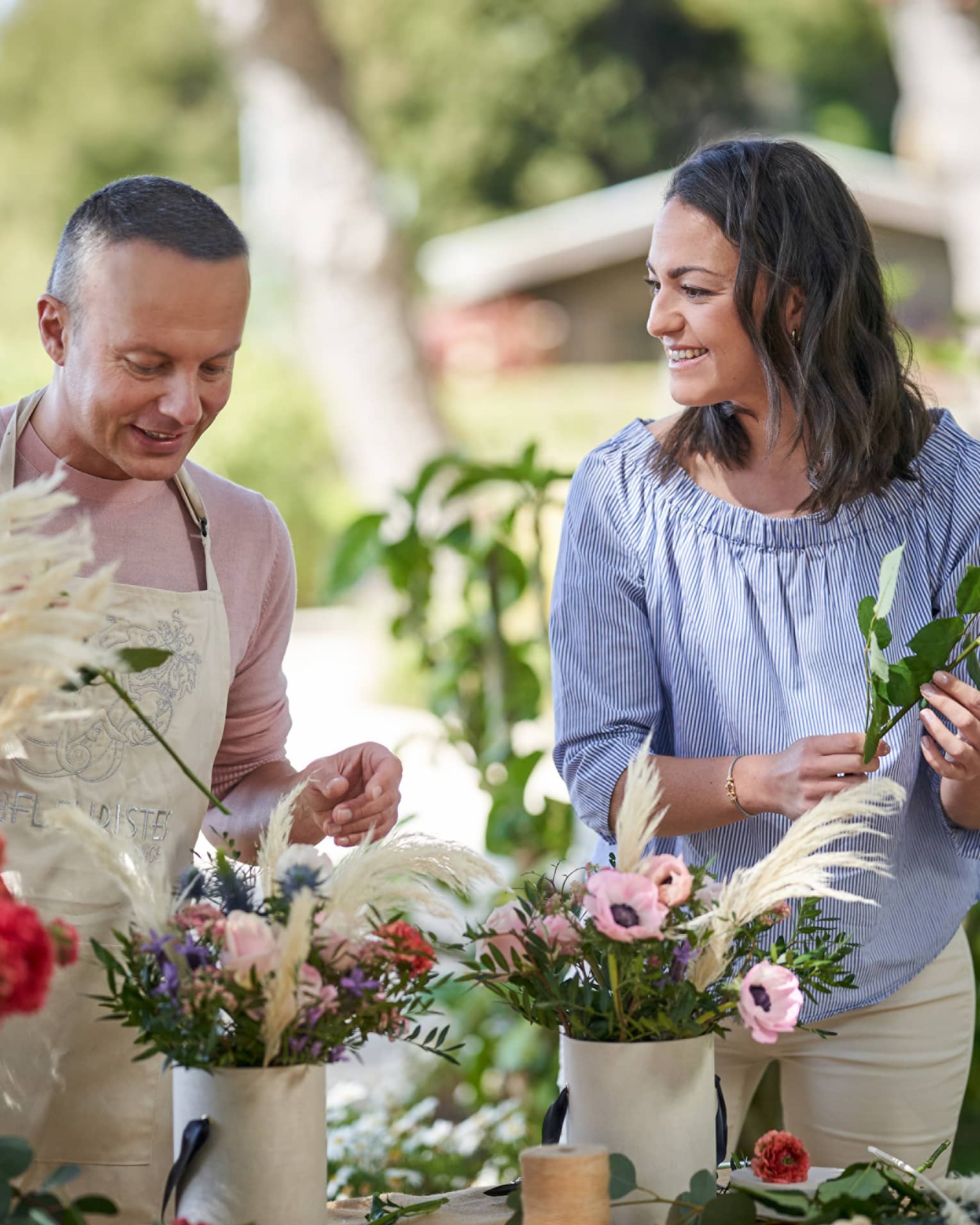 Two people stand outside at a table putting together floral bouquets