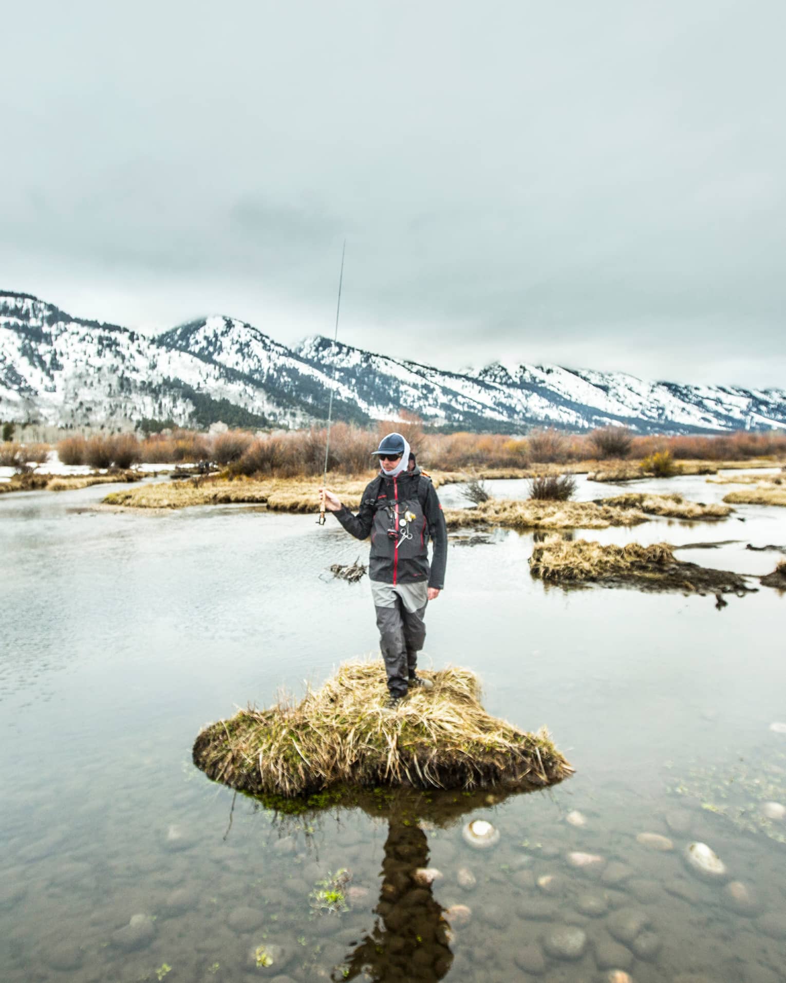 A man standing on a small piece of land surrounded by water holding a fishing rod.