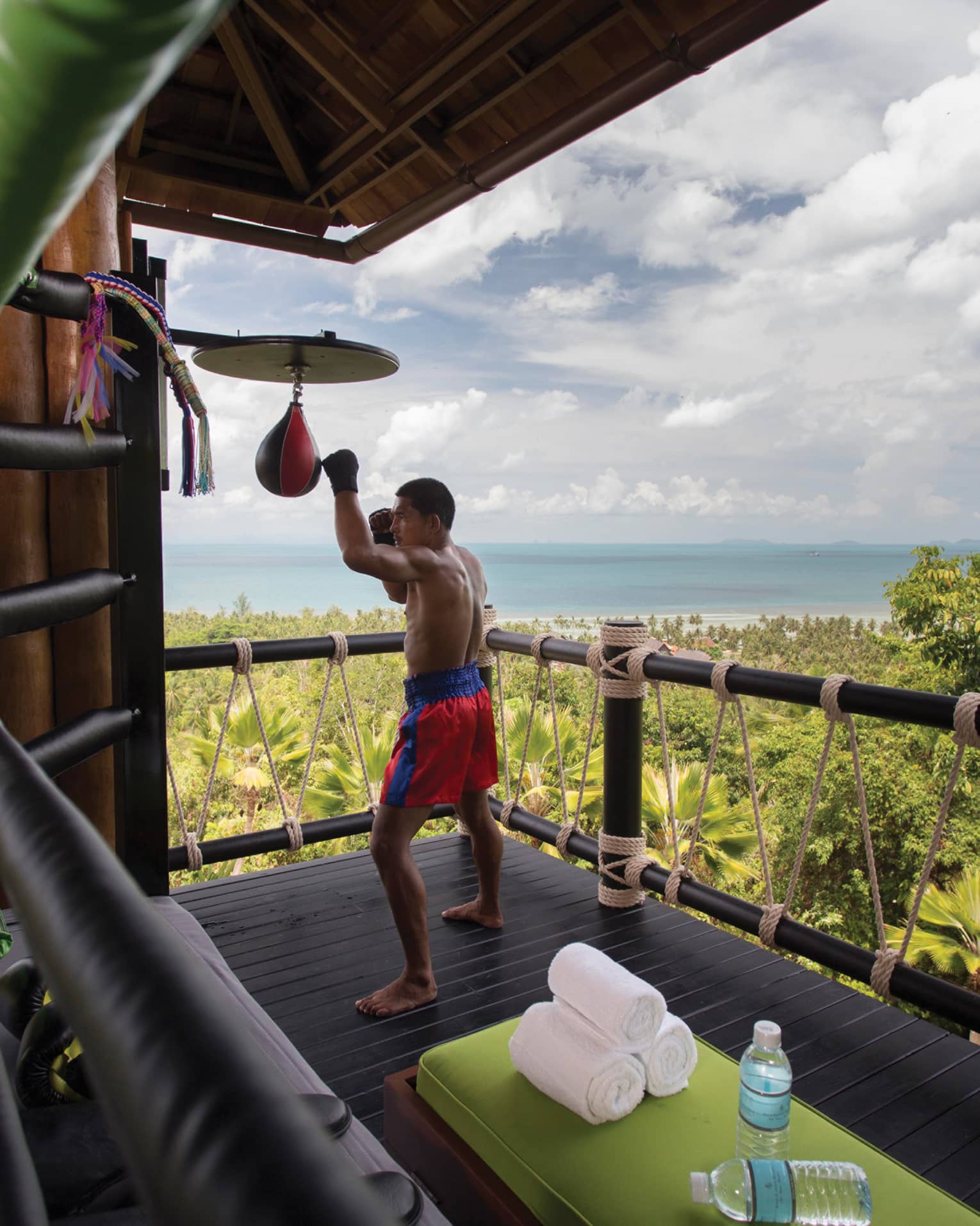 Muay Thai boxer hitting bags on wood deck high up on mountain