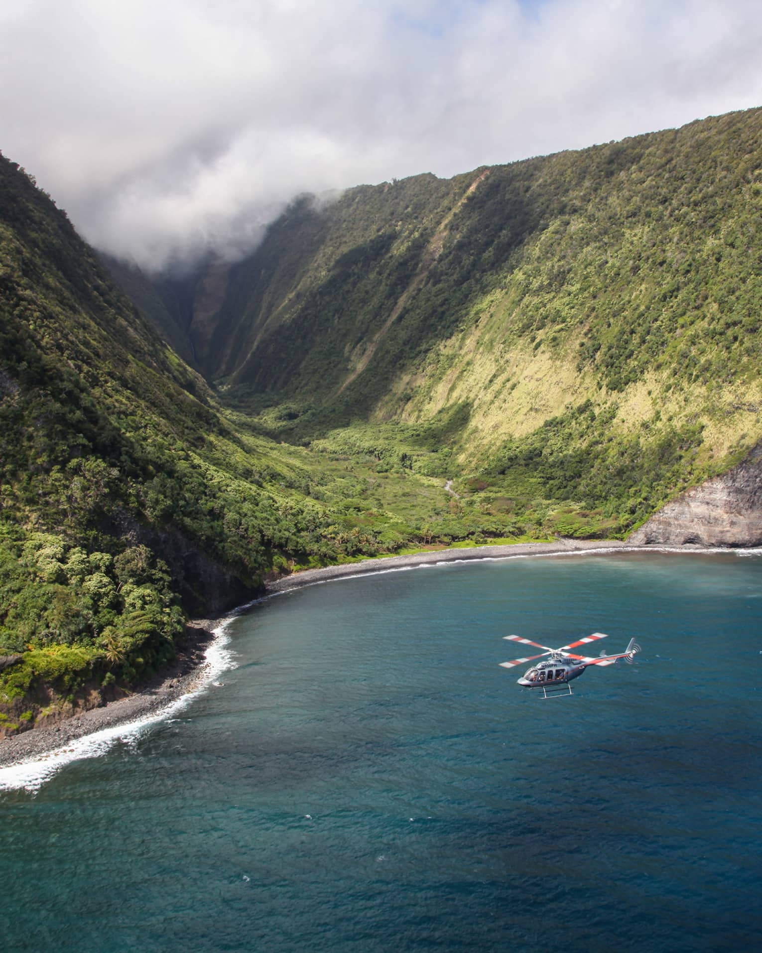 Helicopter flies over ocean by sweeping green volcanic mountains