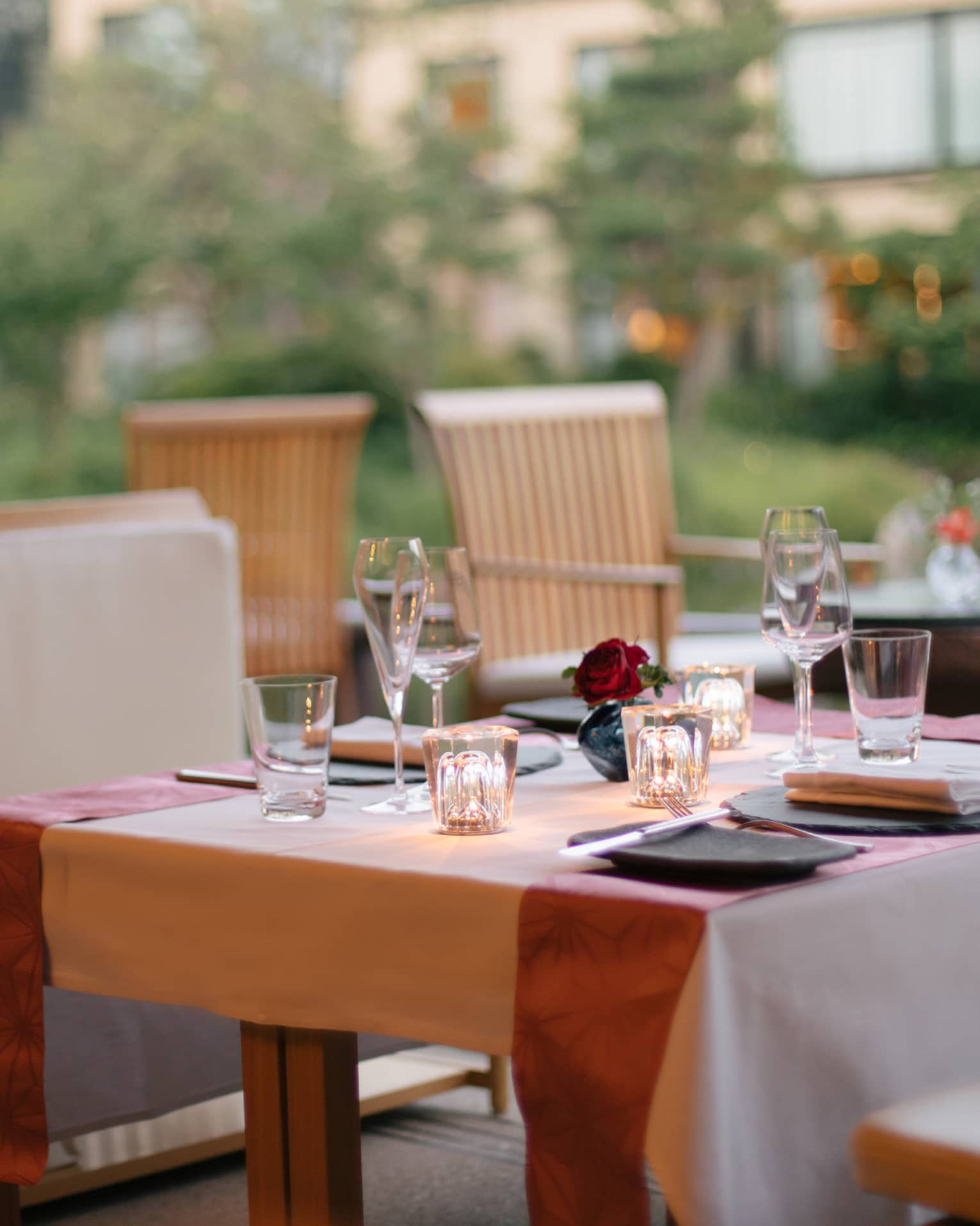 Elegant outdoor dining table set with wine glasses, a small red rose centerpiece and soft lighting at Four Seasons 