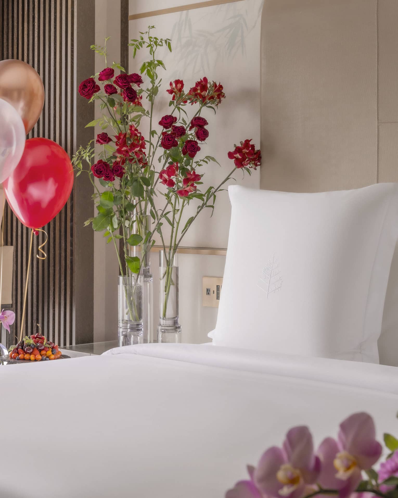 King bed with white linens surrounded by colourful balloons and ice bucket of champagne nearby
