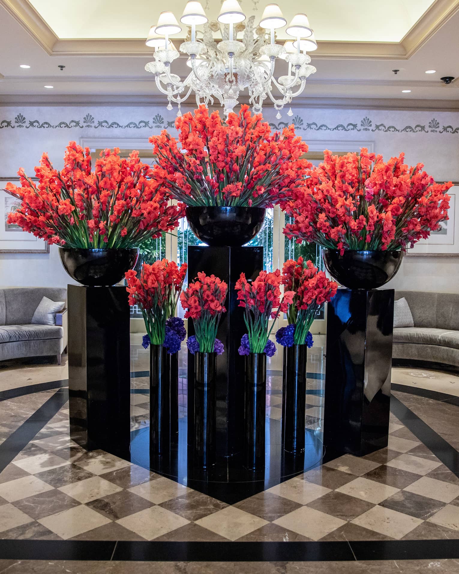 Hotel lobby, large red floral arrangements in black vases under crystal chandelier