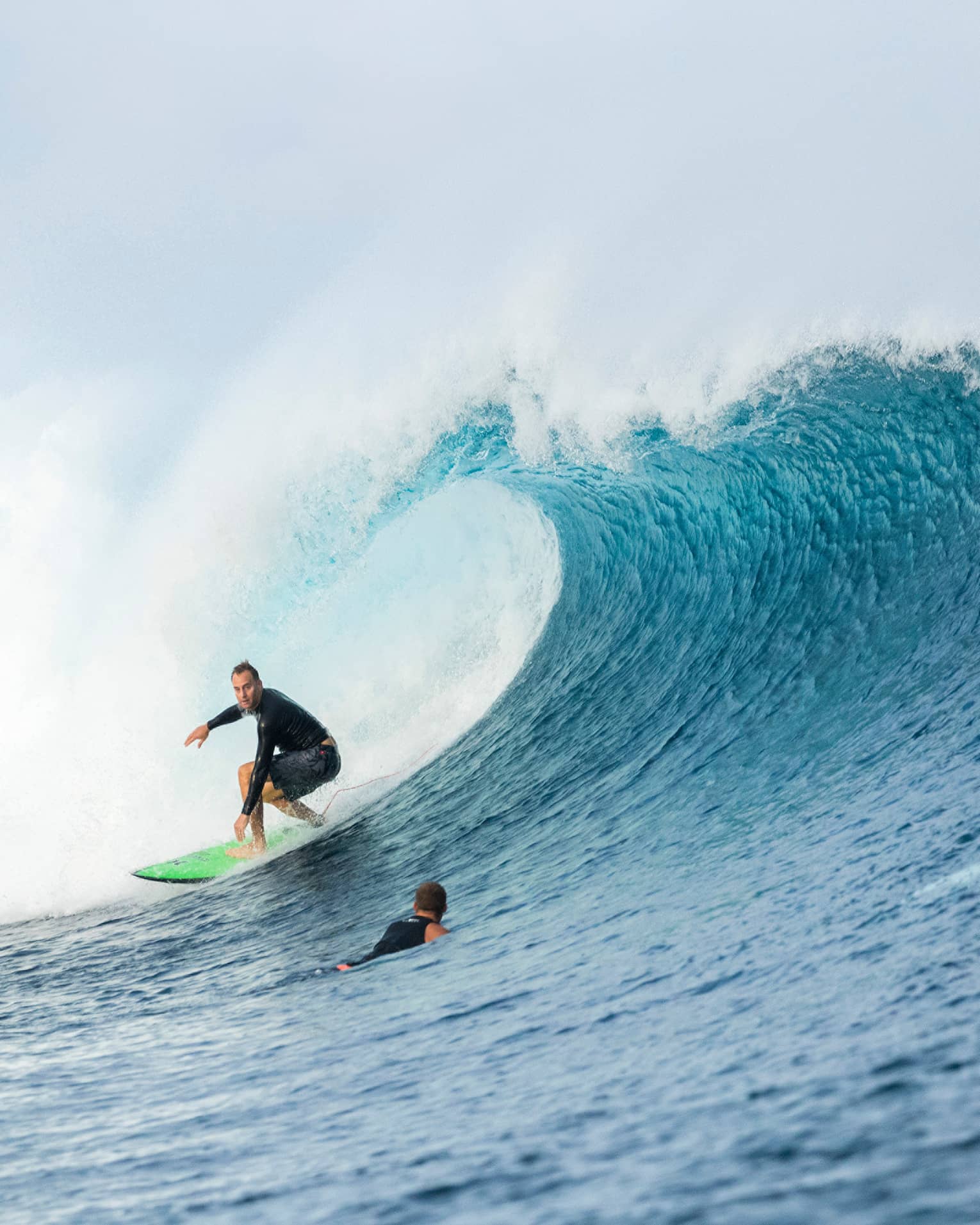 Surfer rides surfboard on large wave, two surfers swimming in water