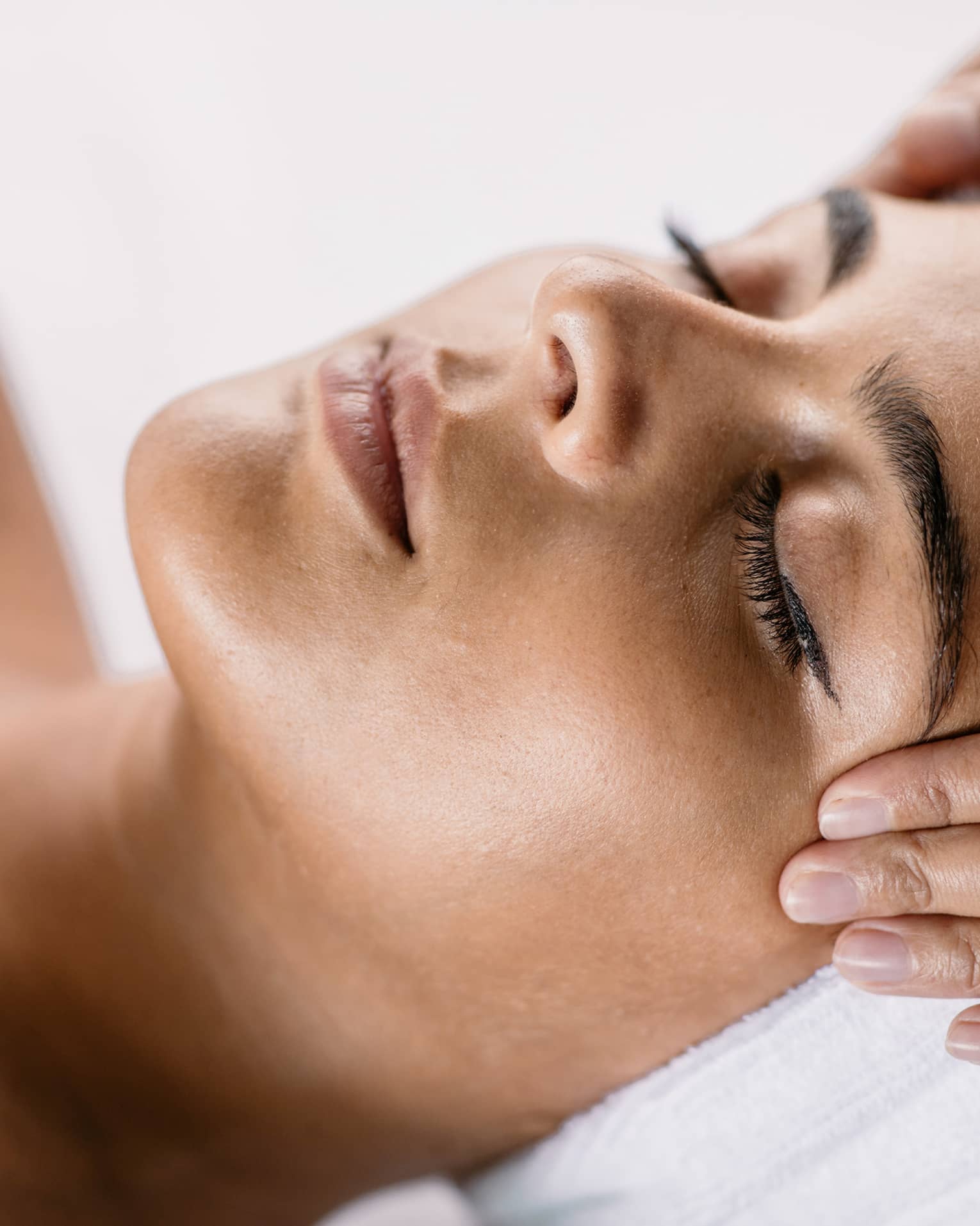 Hands massage woman's temples as she closes her eyes, spa towel around hair