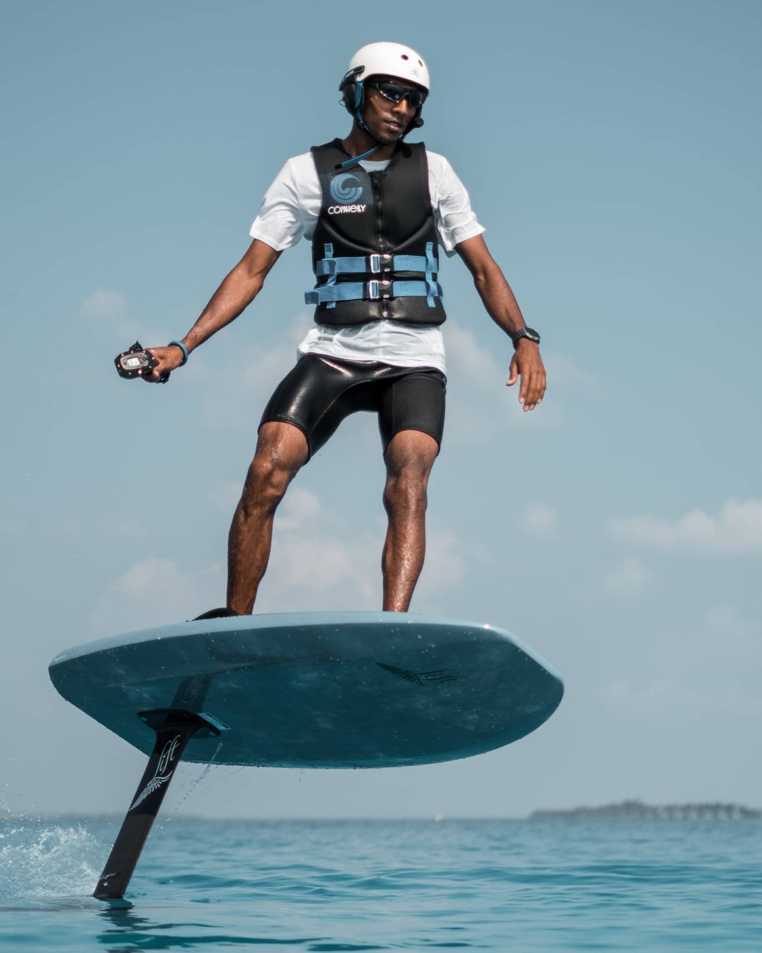 In a helmet and life jacket, an adventurer stands on an eFoil using a handheld control to propel the board out of the water.