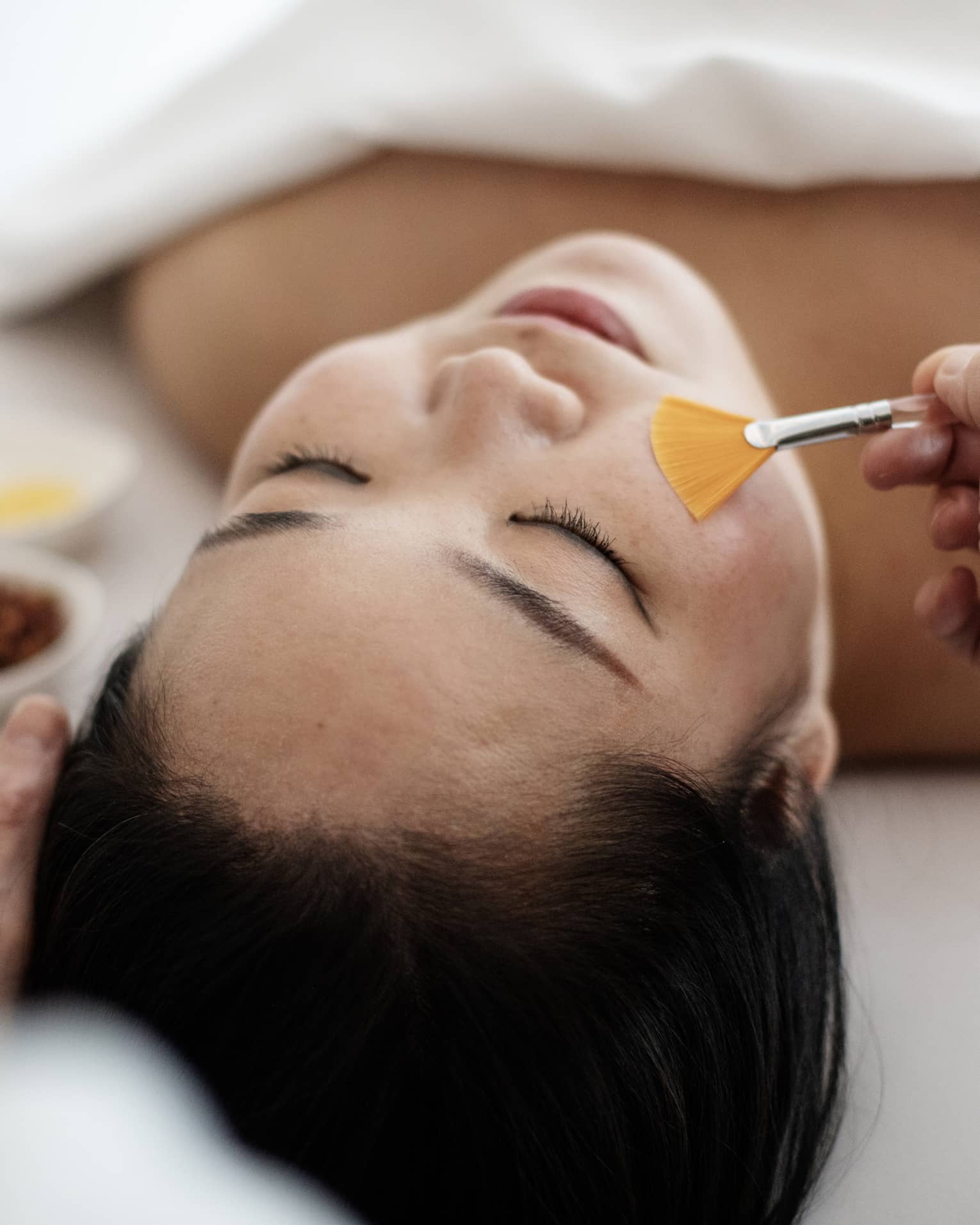 A woman receiving a spa treatment utilizing a brush on her face.