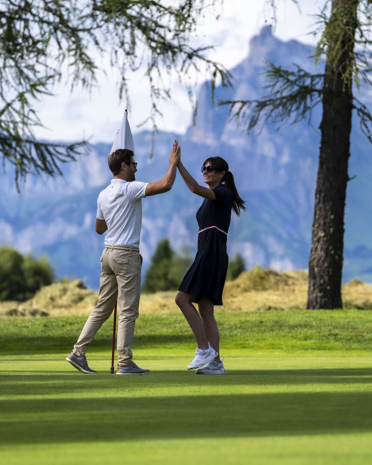 Two people high-fiving on a golf course with mountains in the distance
