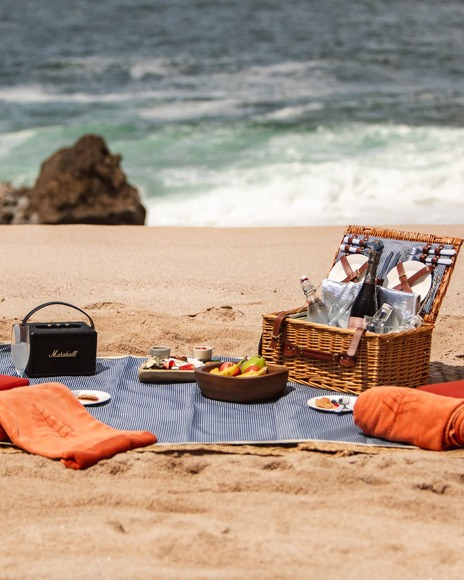 A picnic basket with cushions and a blanket on a beach.