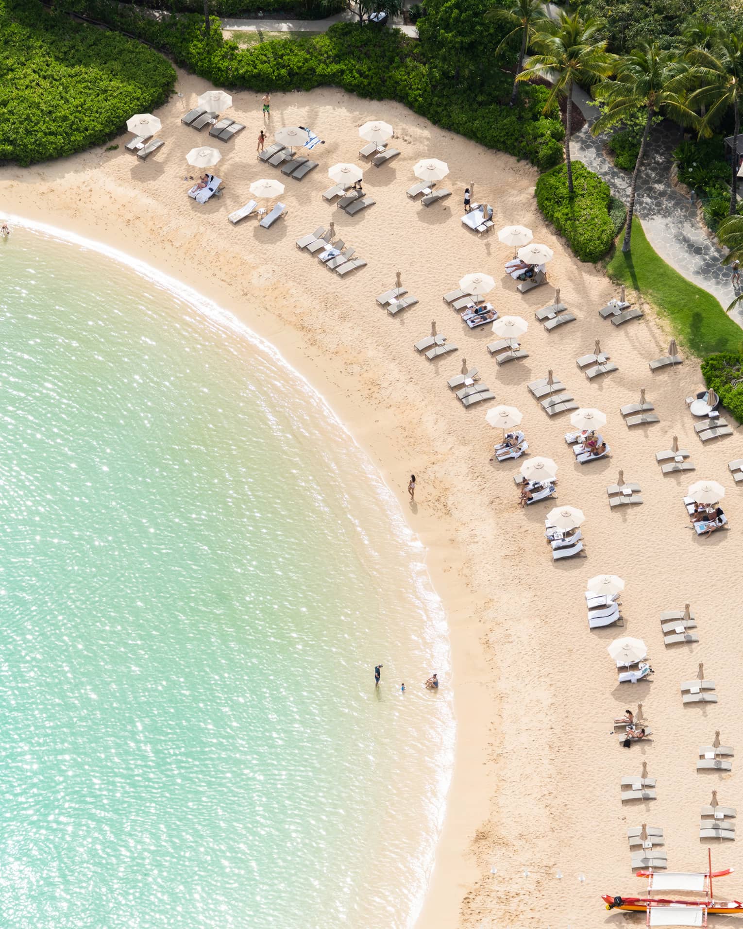 Aerial view of curved beach and clear blue water, beach chairs, resort pool