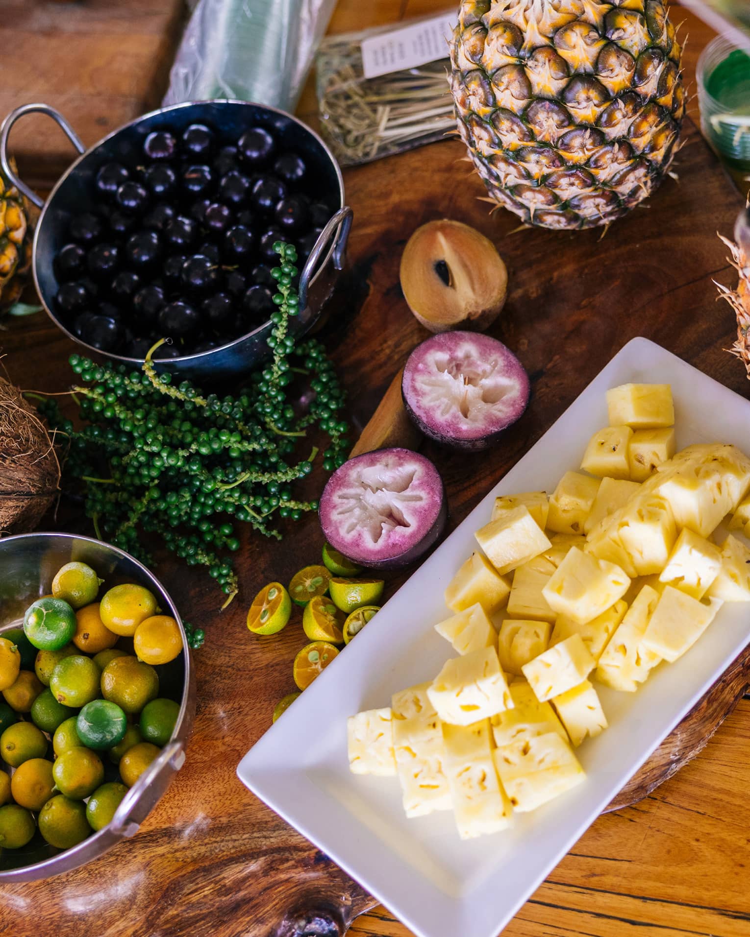 Table set with plate of cubed pineapple, bowl of berries, a halved coconut and other fruits