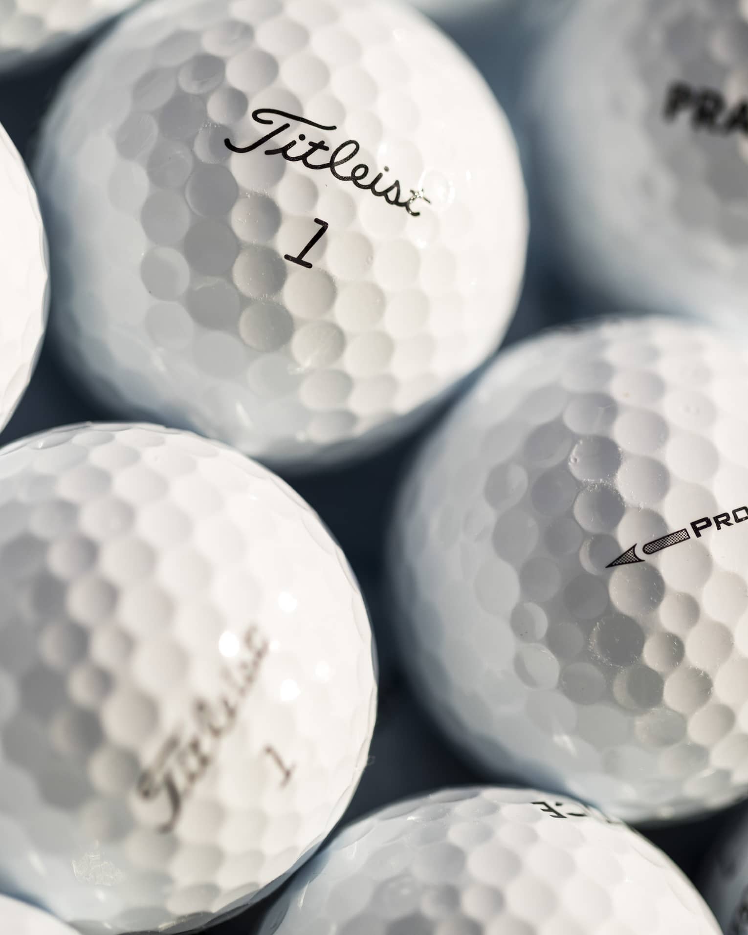 Close-up of white golf balls, each labeled with either Practice, Pro V1, or Titleist 1 in black font.