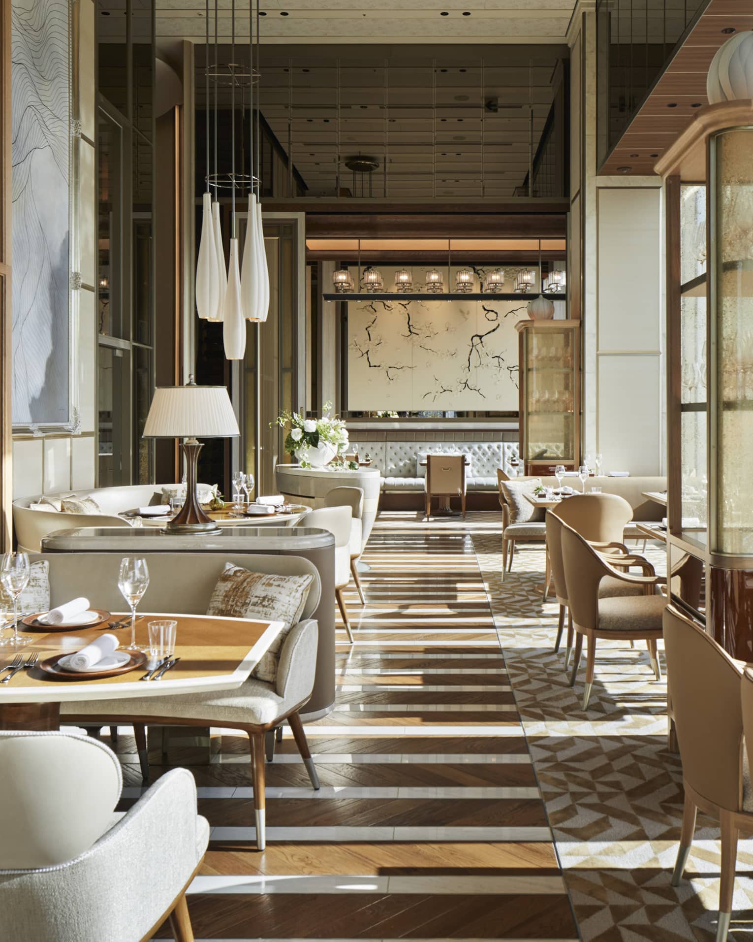 Est dining room with cream plush chairs, tables set with glassware, natural light, hardwood floors