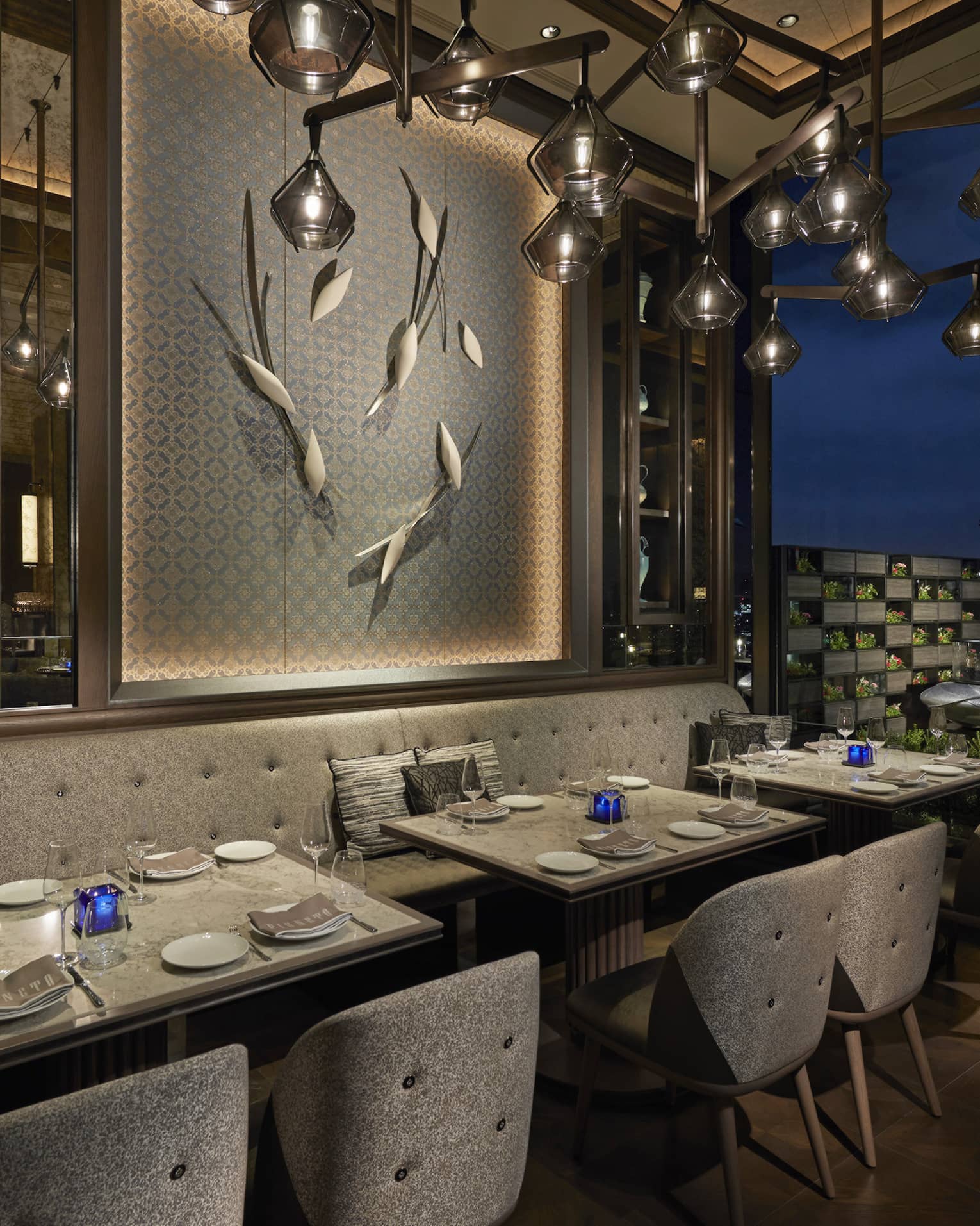 Tables set for two overlook nighttime skyline, floor-to-ceiling windows, intimate lighting, grey colour scheme