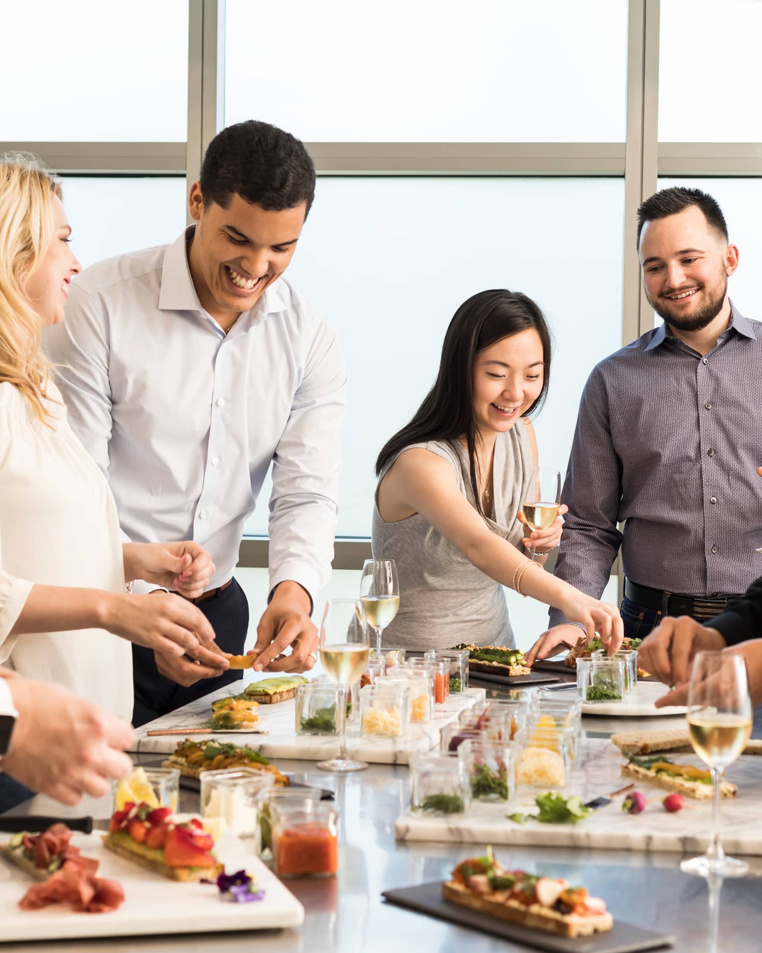 People stand, socialize, drink wine around table with appetizer boards