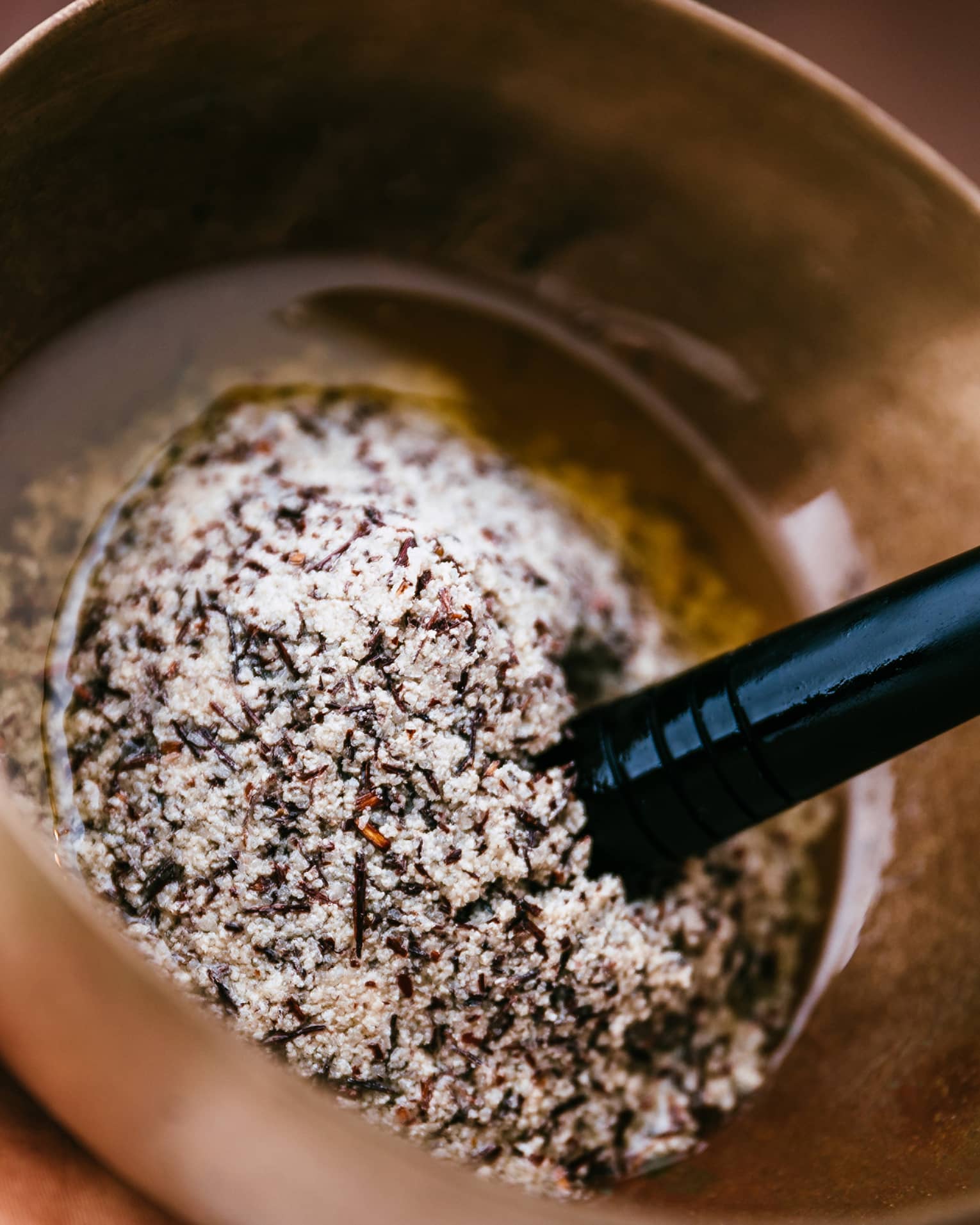 A person uses a golden mortar and pestle to grind several salts and spices into oil.