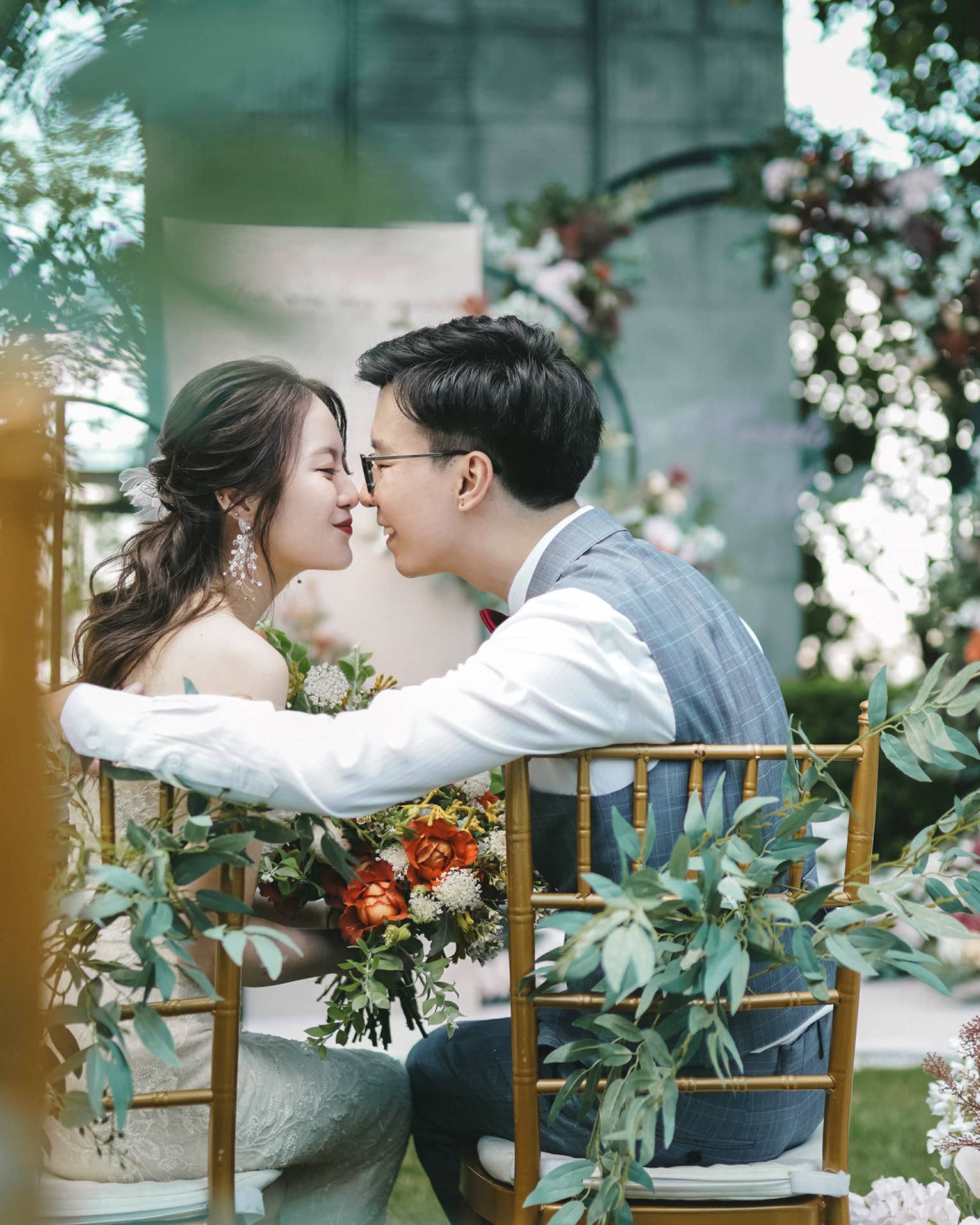 Bride and groom lean in for a kiss at garden wedding dining table surrounded by flowers