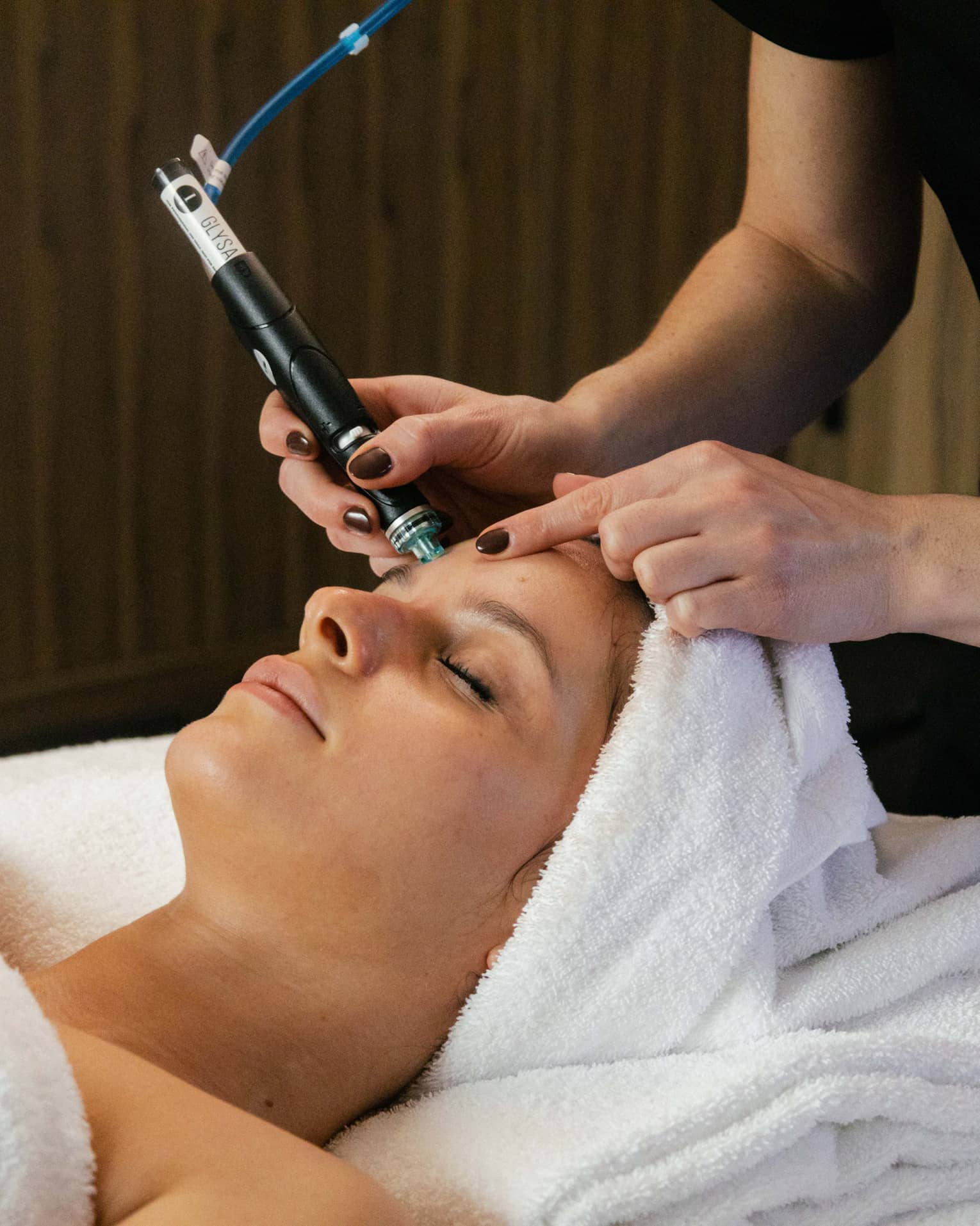 A guest laying on a spa table with a towel wrapped around their hair and getting a facial