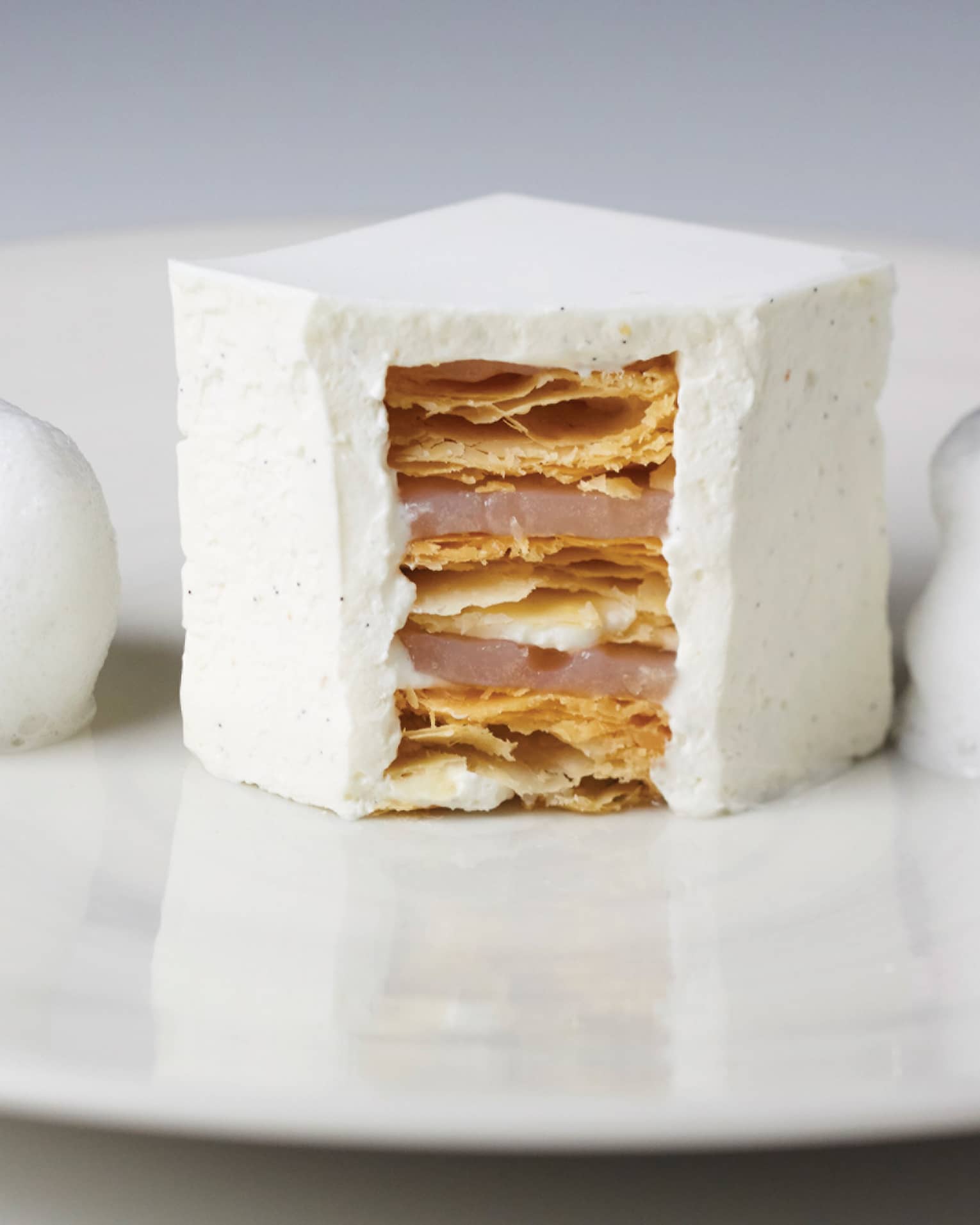 White foam flanks white millefeuille cut open in center, showing layers on white plate