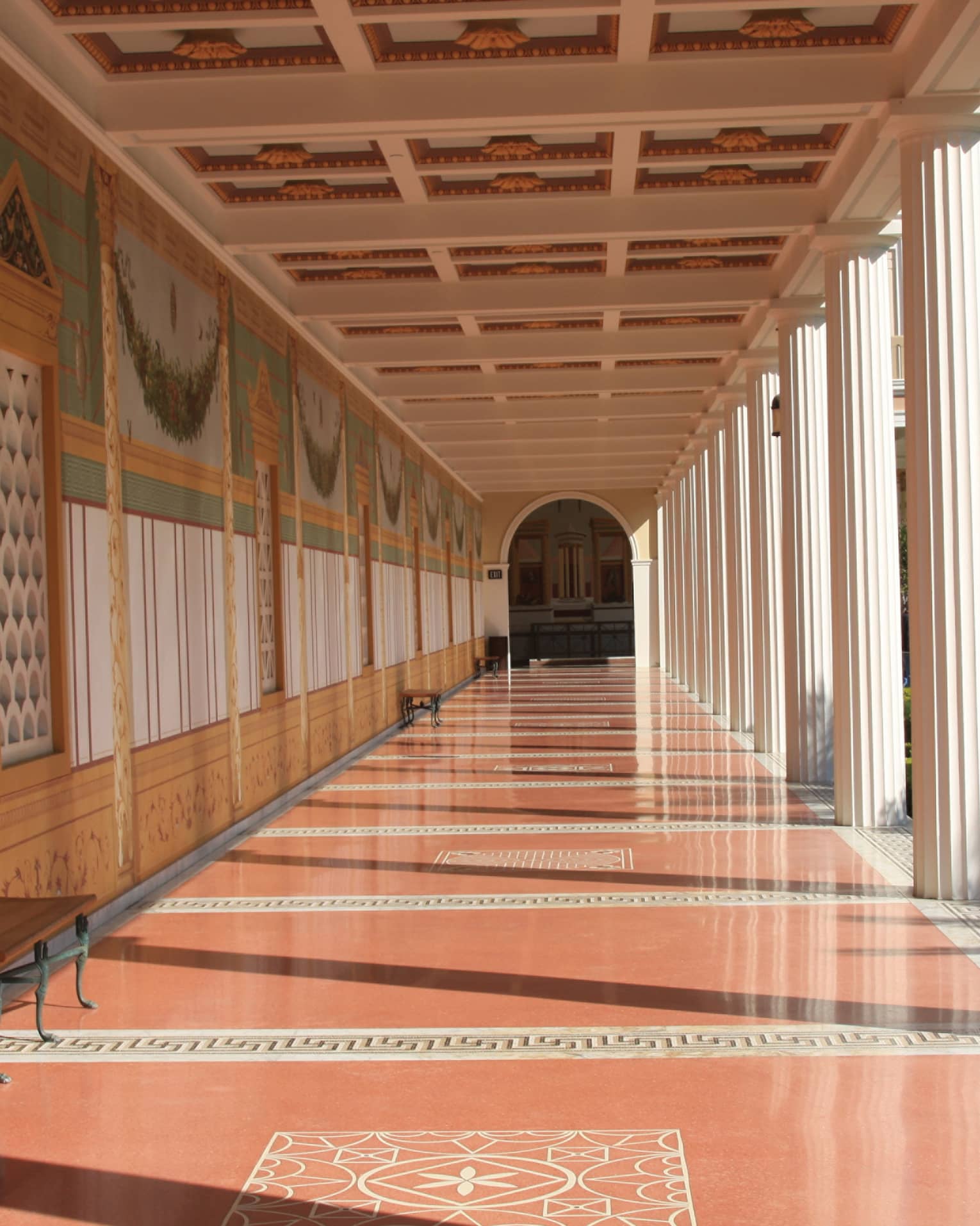 A long hallway with orange floors and columns on the side leading to an arched doorway.