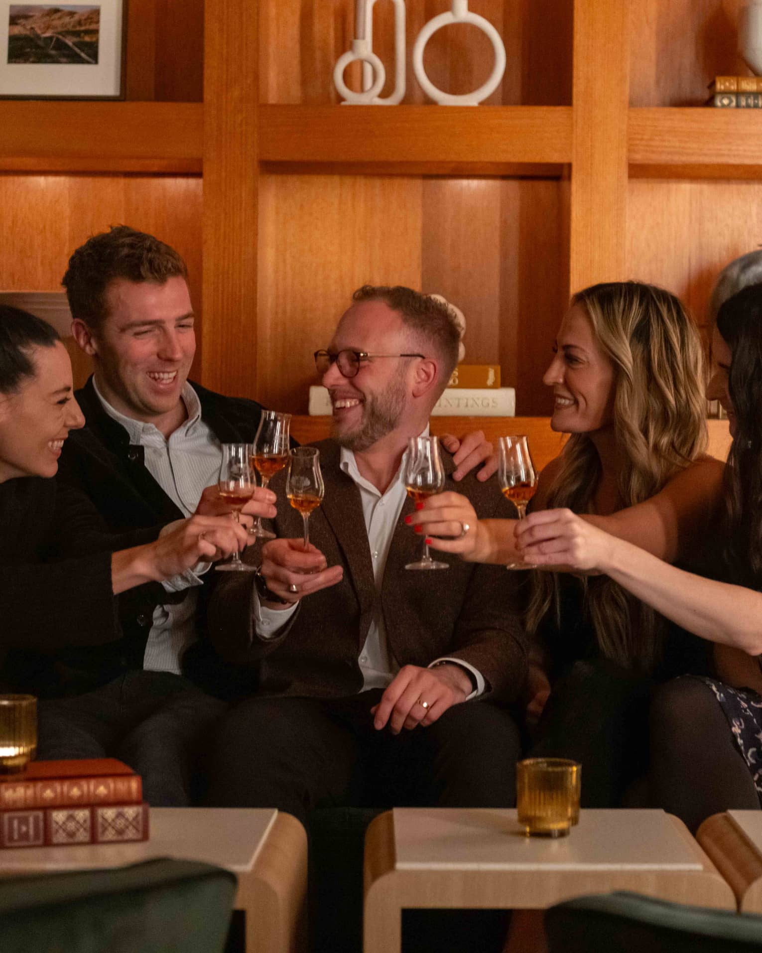 Group of smiling friends on couch raise their glasses in a toast