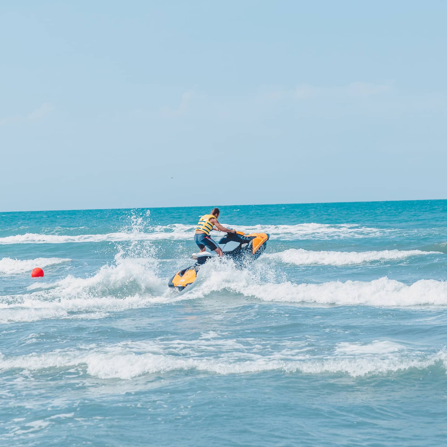 Person riding jet ski along waves in blue ocean